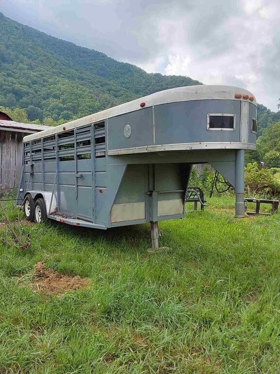 Gray livestock trailer parked on grass with mountain backdrop