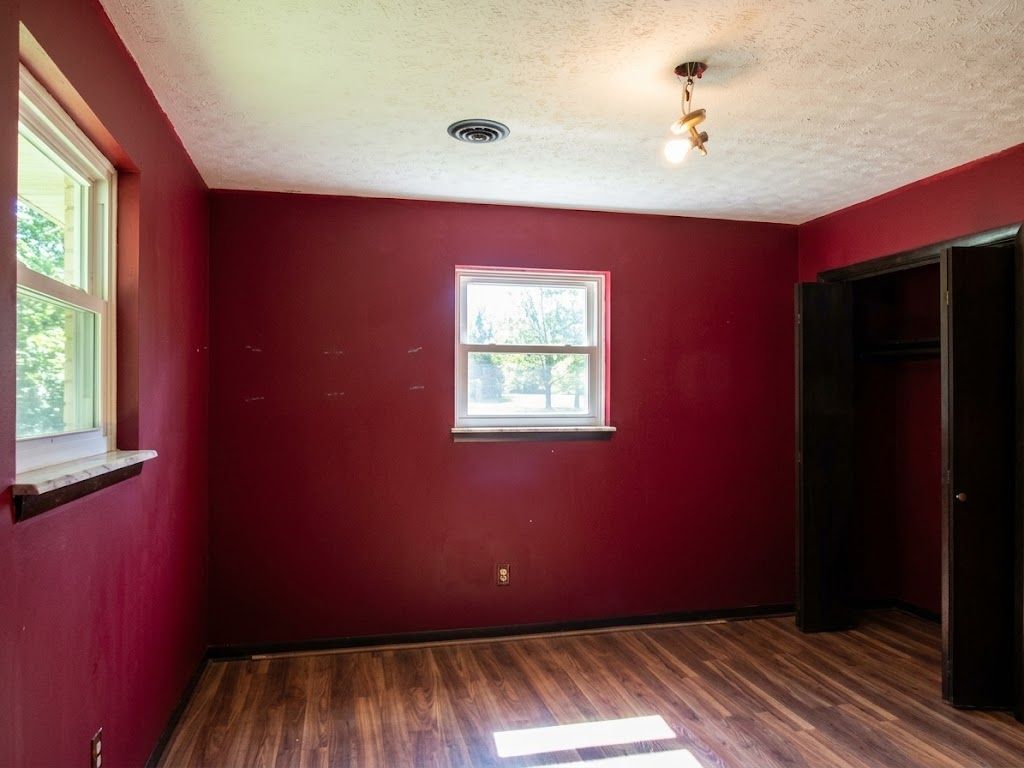 Empty room with dark red walls, two windows, hardwood floor, and an open closet door.