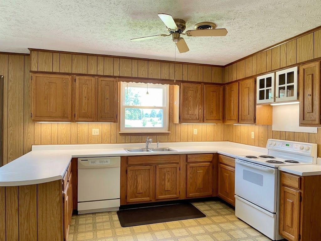 Wood-paneled kitchen with white countertops, cabinets, stove, and a window over the sink.