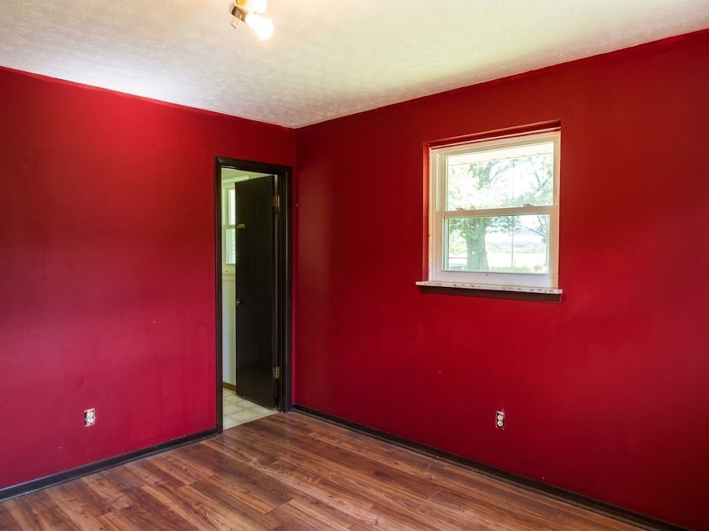 Empty red-painted room with wood floor, open doorway, and a small window letting in daylight