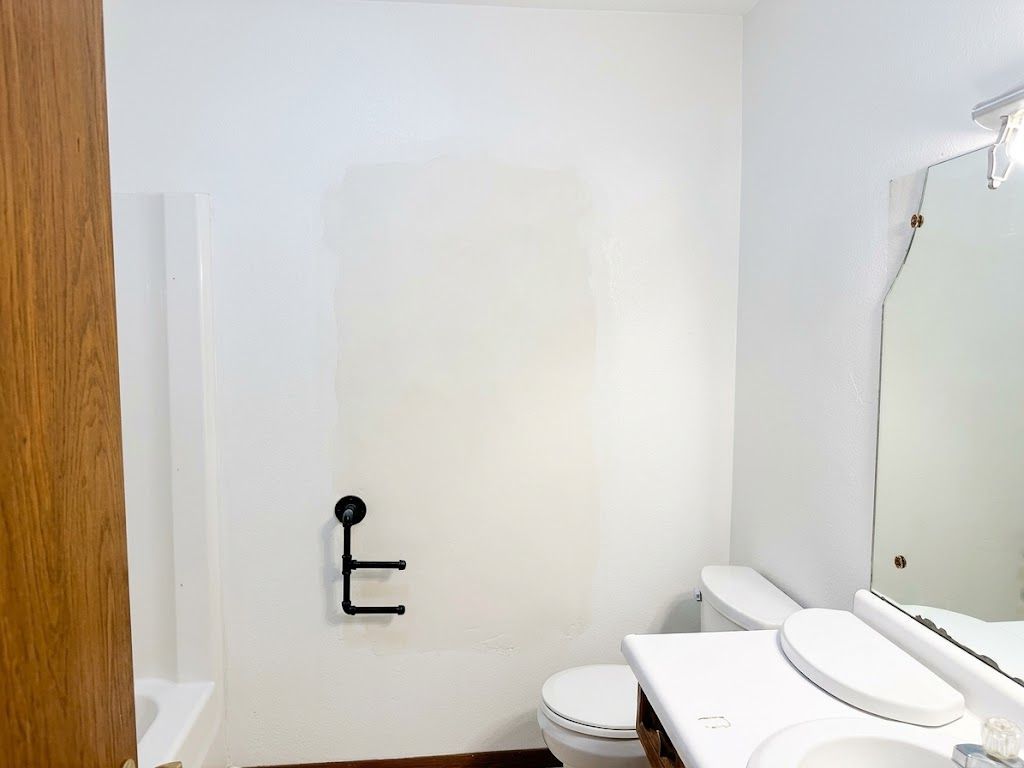 Small white bathroom with toilet, sink, mirror, bathtub, and black toilet paper holder on the wall