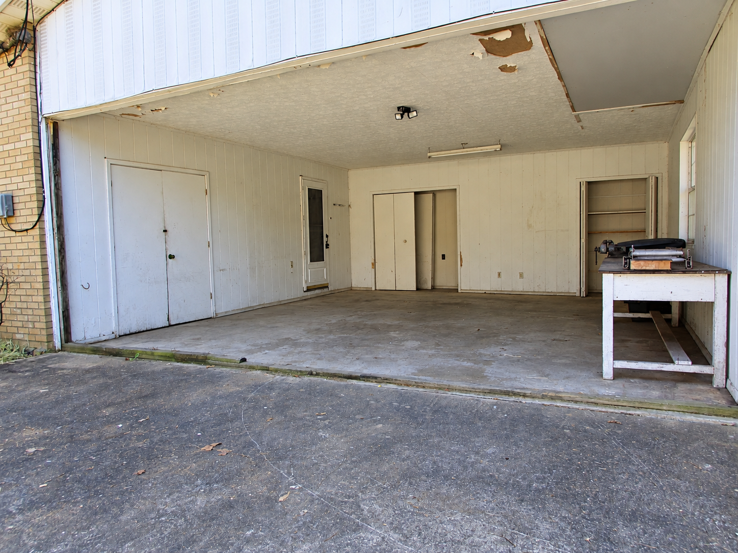 Empty open garage with white walls, concrete floor, and a workbench on the right.