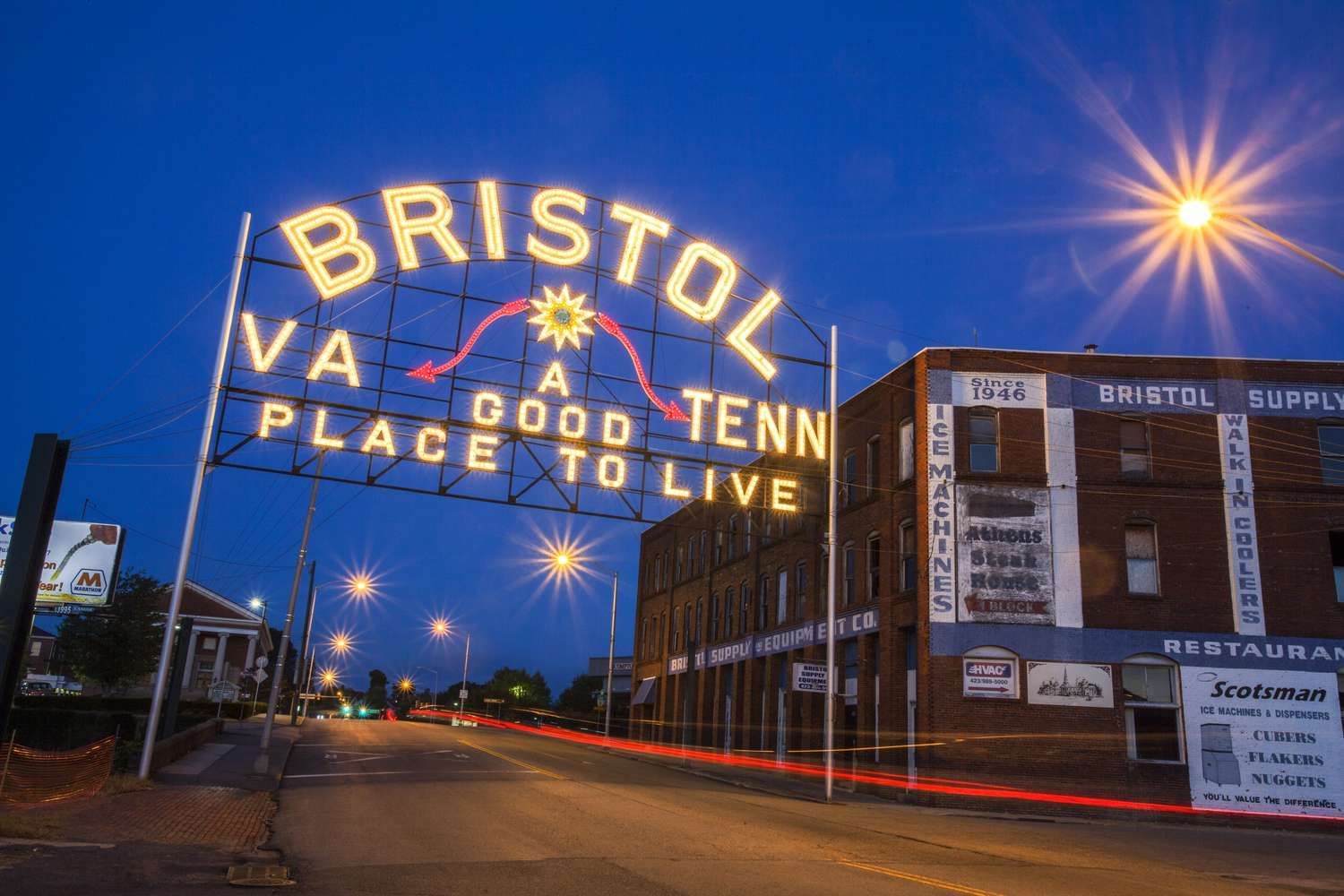 A sign that says Bristol TN/VA a good tenn place to live lit up at night arching over State Street in Bristol