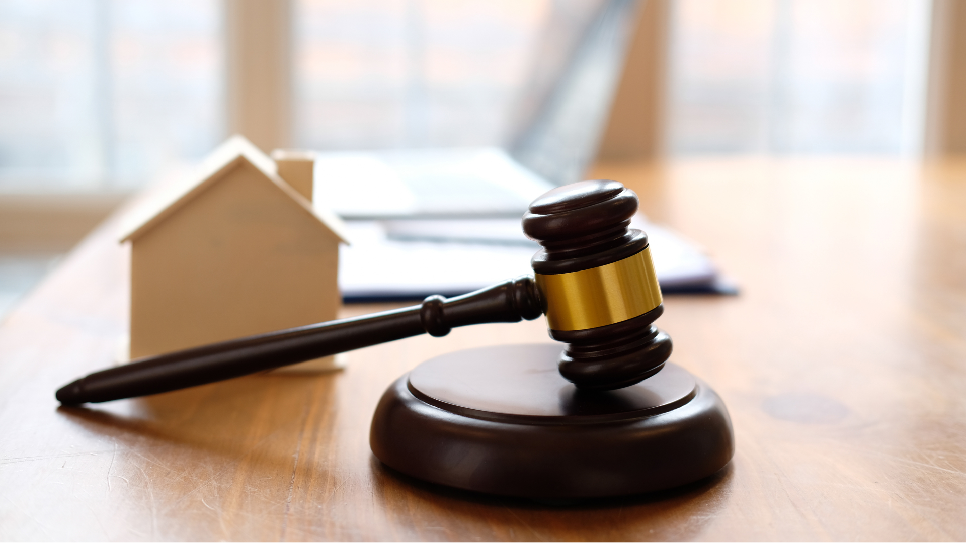 Start an Auction! Wooden gavel on stand next to a small house model, laptop, and documents on a table.