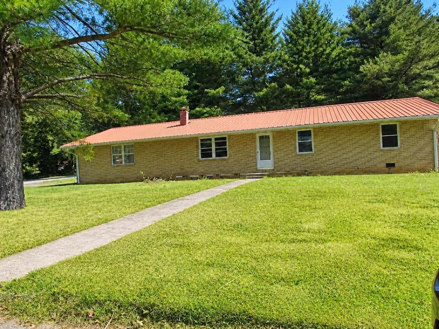 Single-story brick house with red roof, surrounded by green lawn and trees, with a walkway leading to the front.