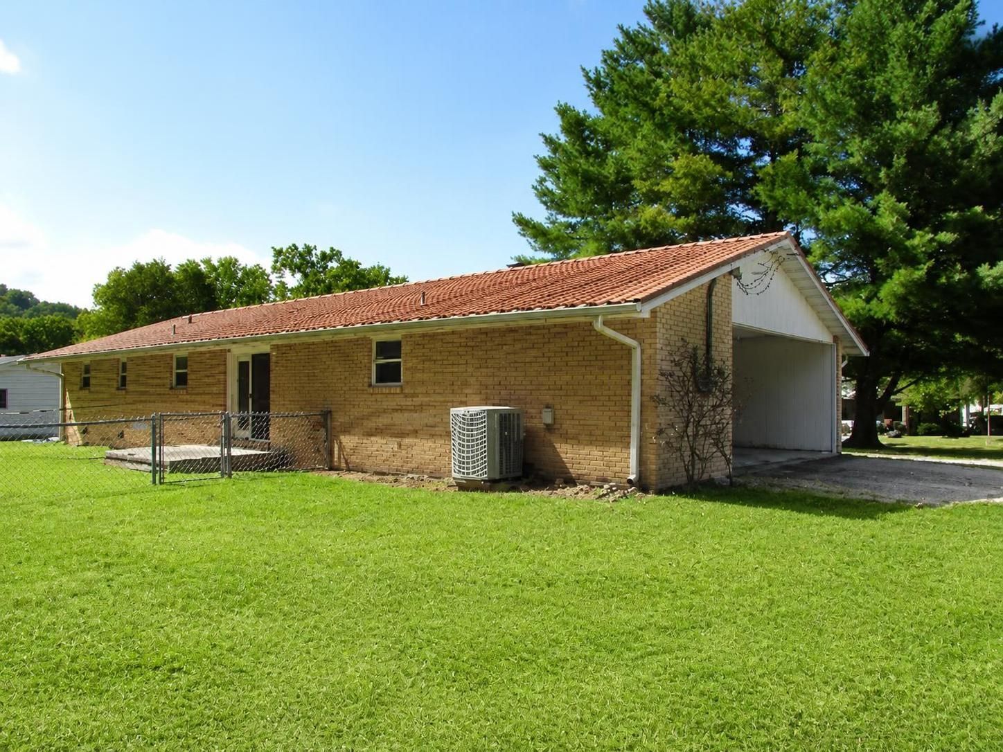 Single-story brick building with red roof and white carport, sitting on a grassy lawn under a blue sky.