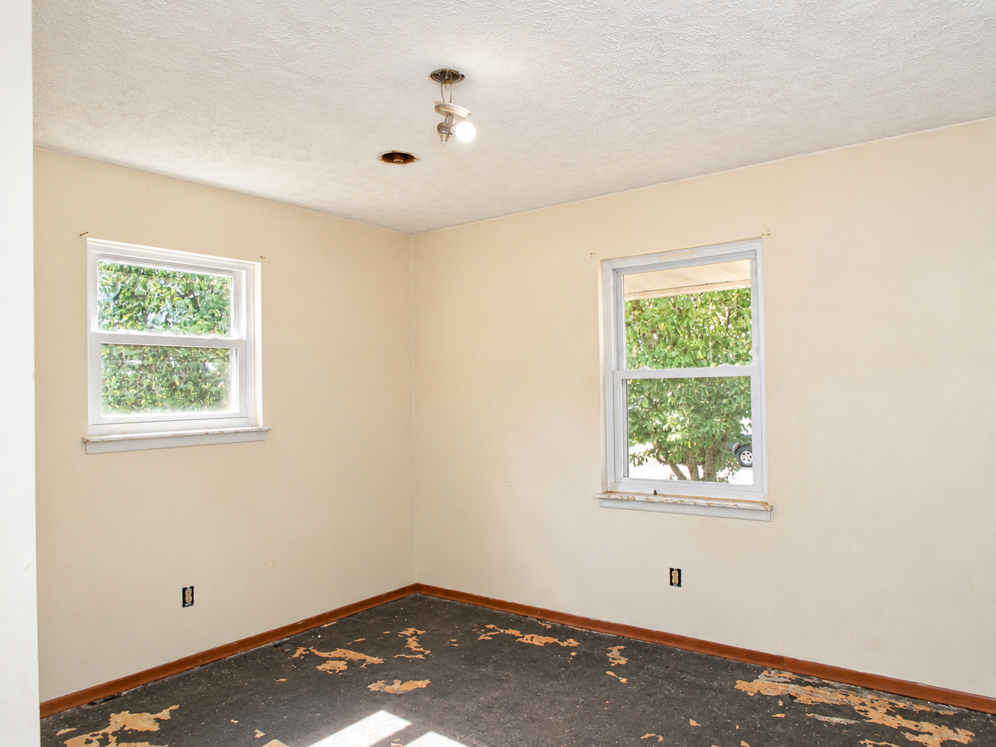 Empty beige room with two windows, white trim, and worn dark carpet tiles