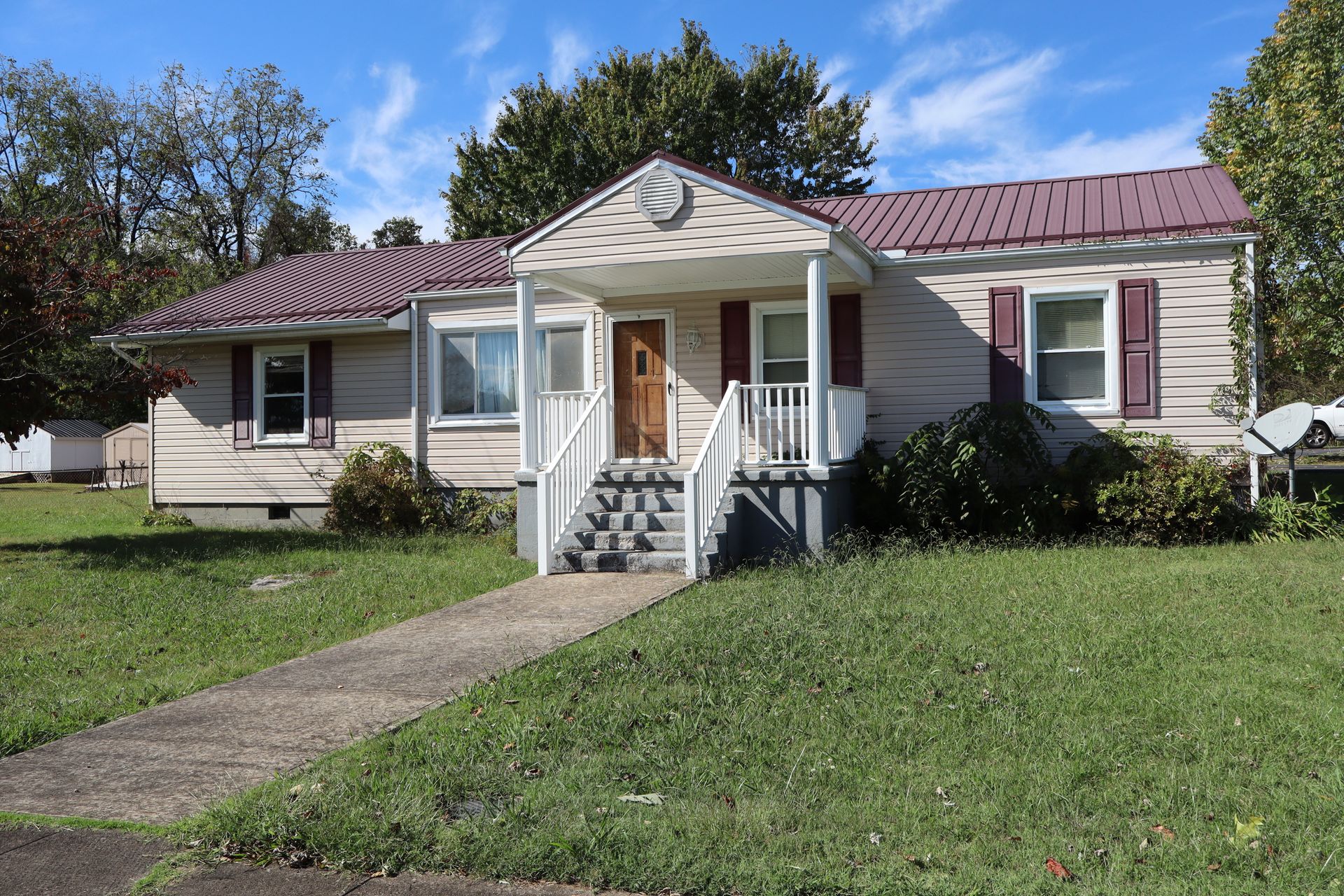 Single-story house with a small front porch, walkway, and green lawn under a blue sky