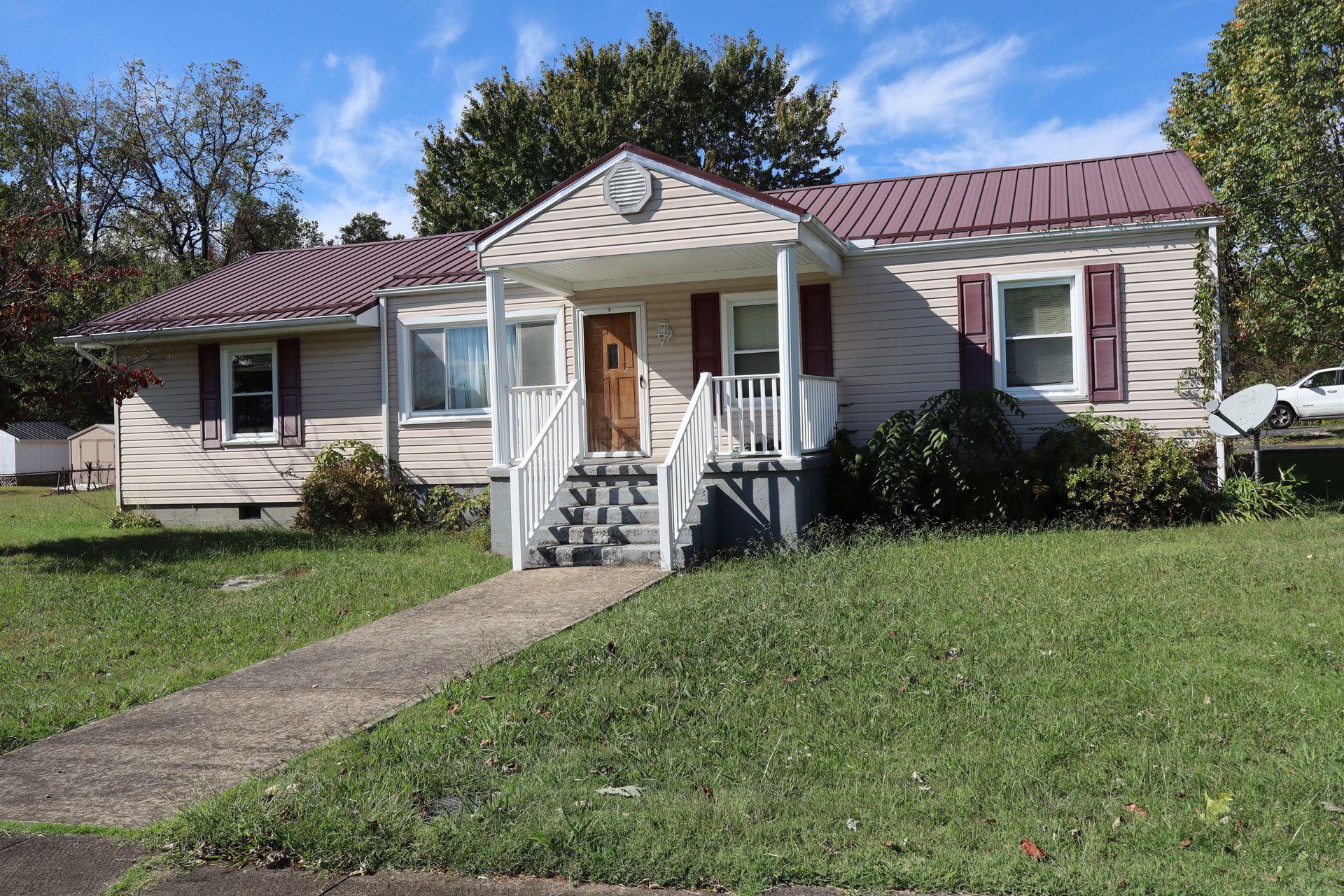 Single-story beige house with red roof, front porch, and a concrete walkway across a green lawn