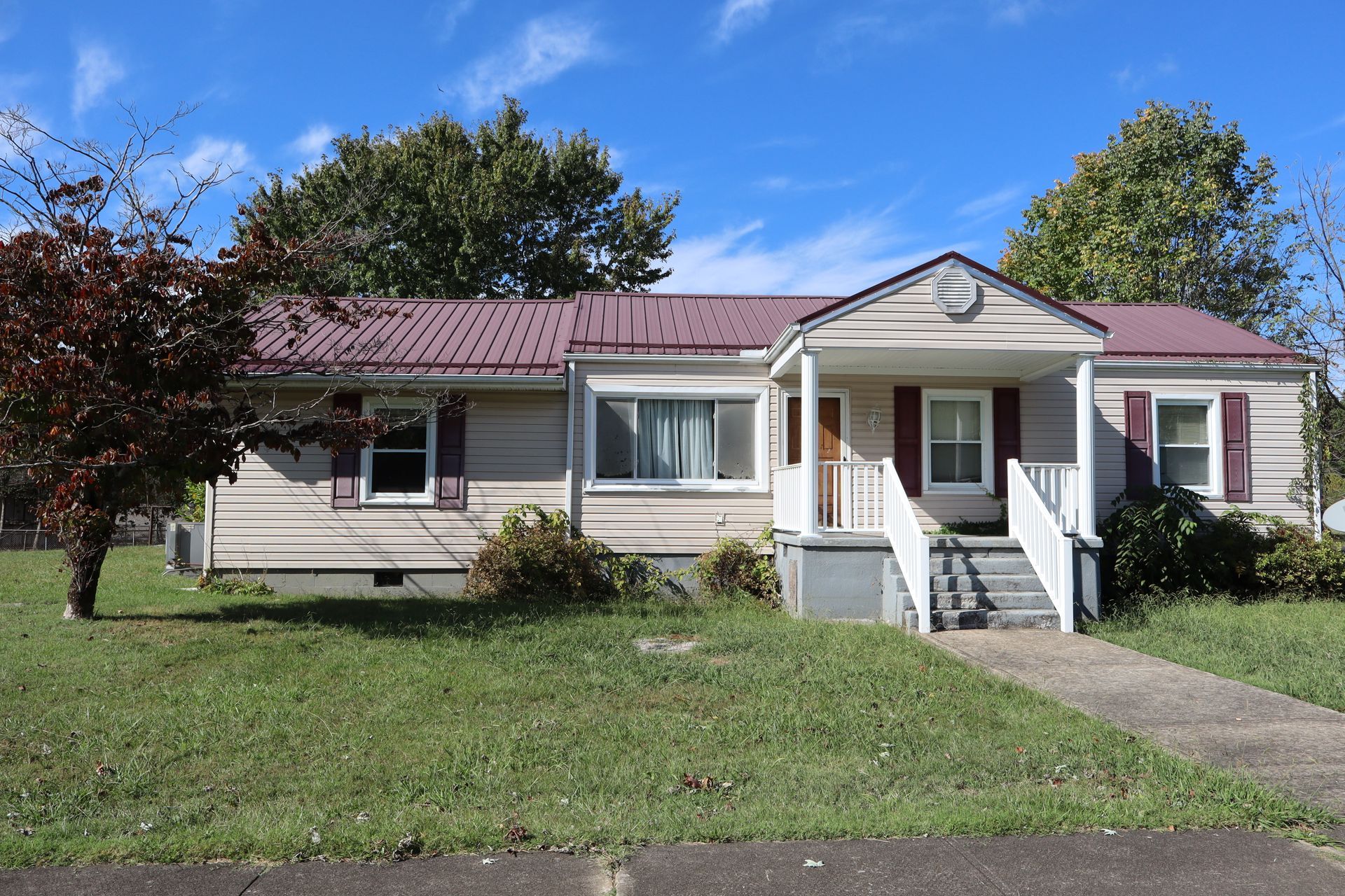 Single-story beige house with red roof and white porch, front lawn and blue sky