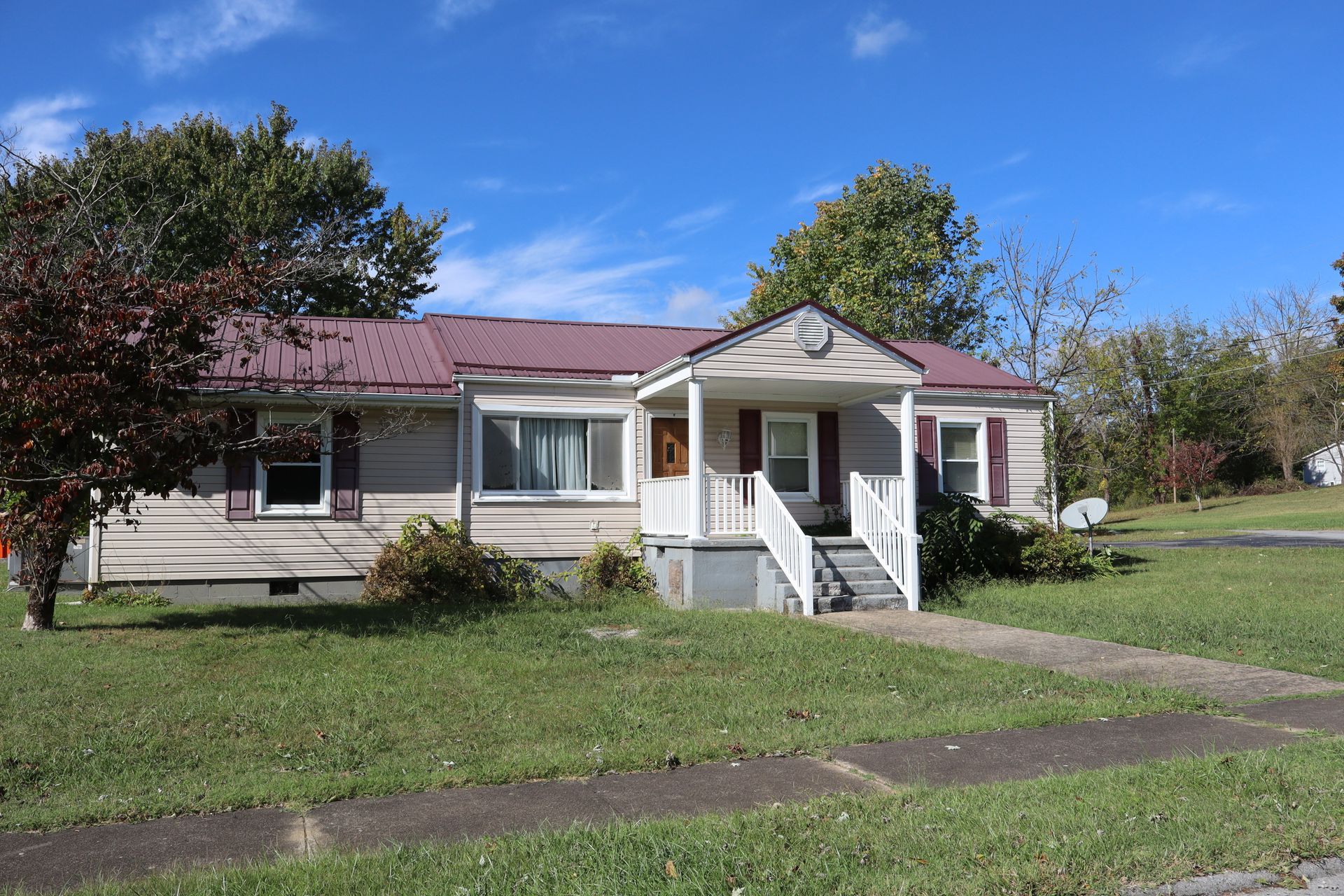 Small beige house with a red roof, white porch steps, and a grassy front yard on a sunny day