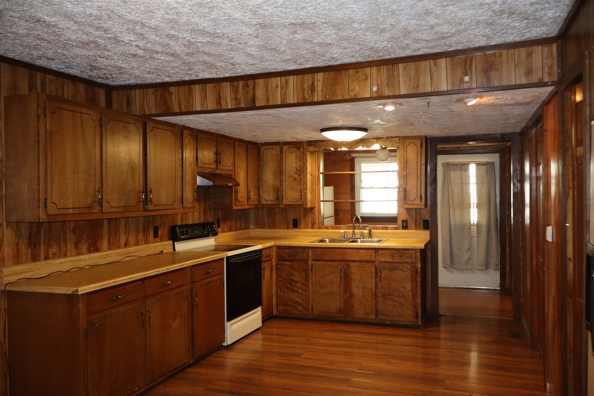 Wood-paneled kitchen with wooden cabinets, white countertops, and a windowed back wall