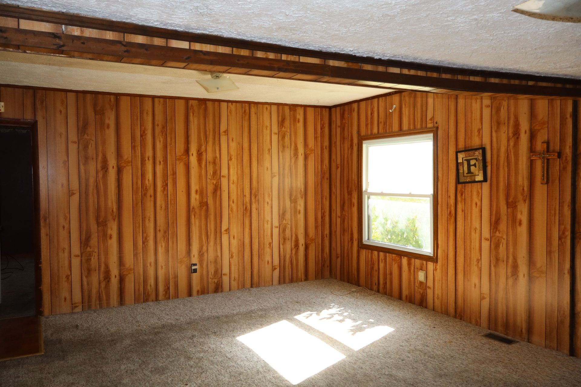 Empty wood-paneled room with a window and sunlight on the carpeted floor.