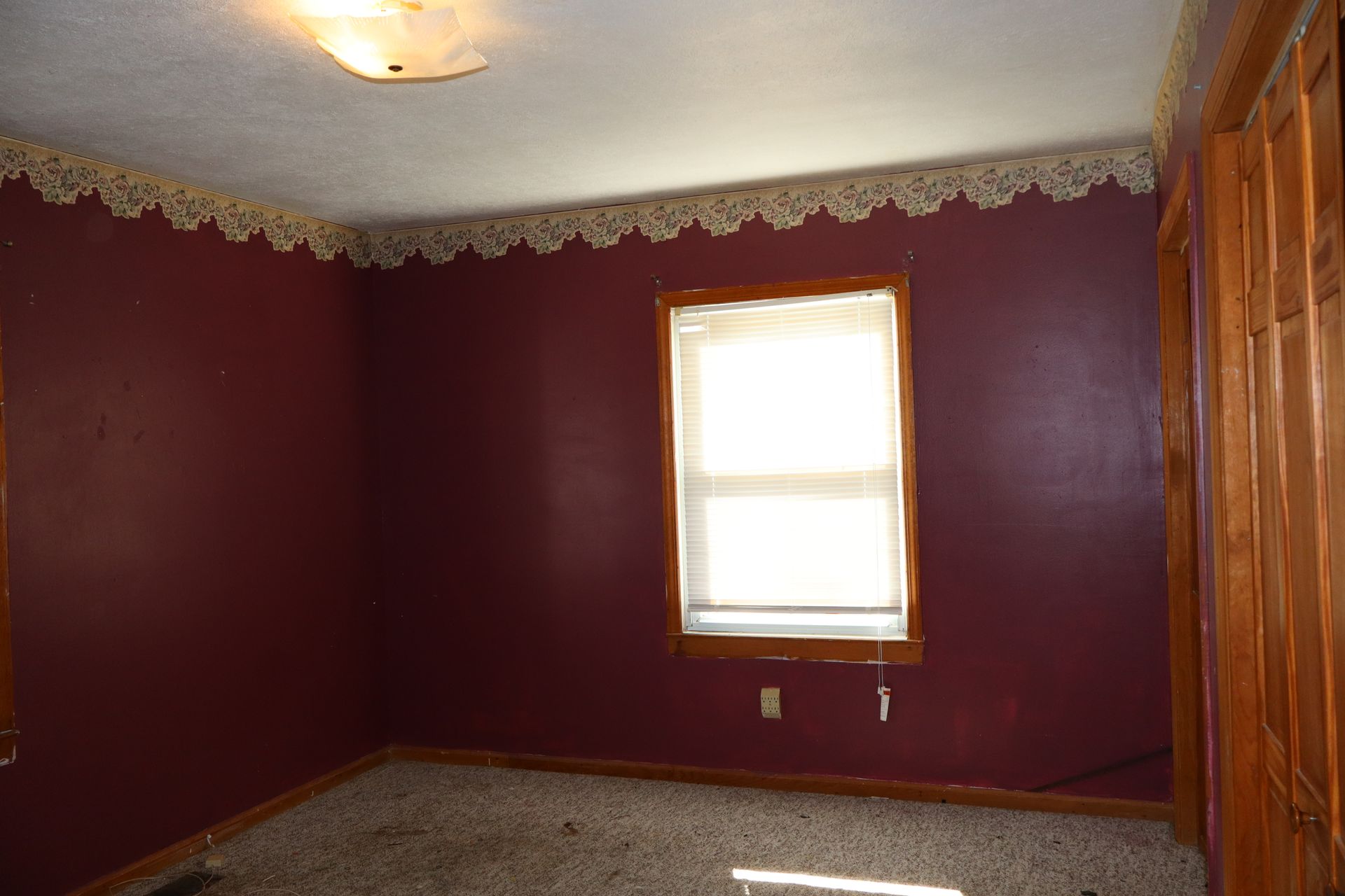 Empty room with burgundy walls, a window, lace trim, and a patterned carpet.