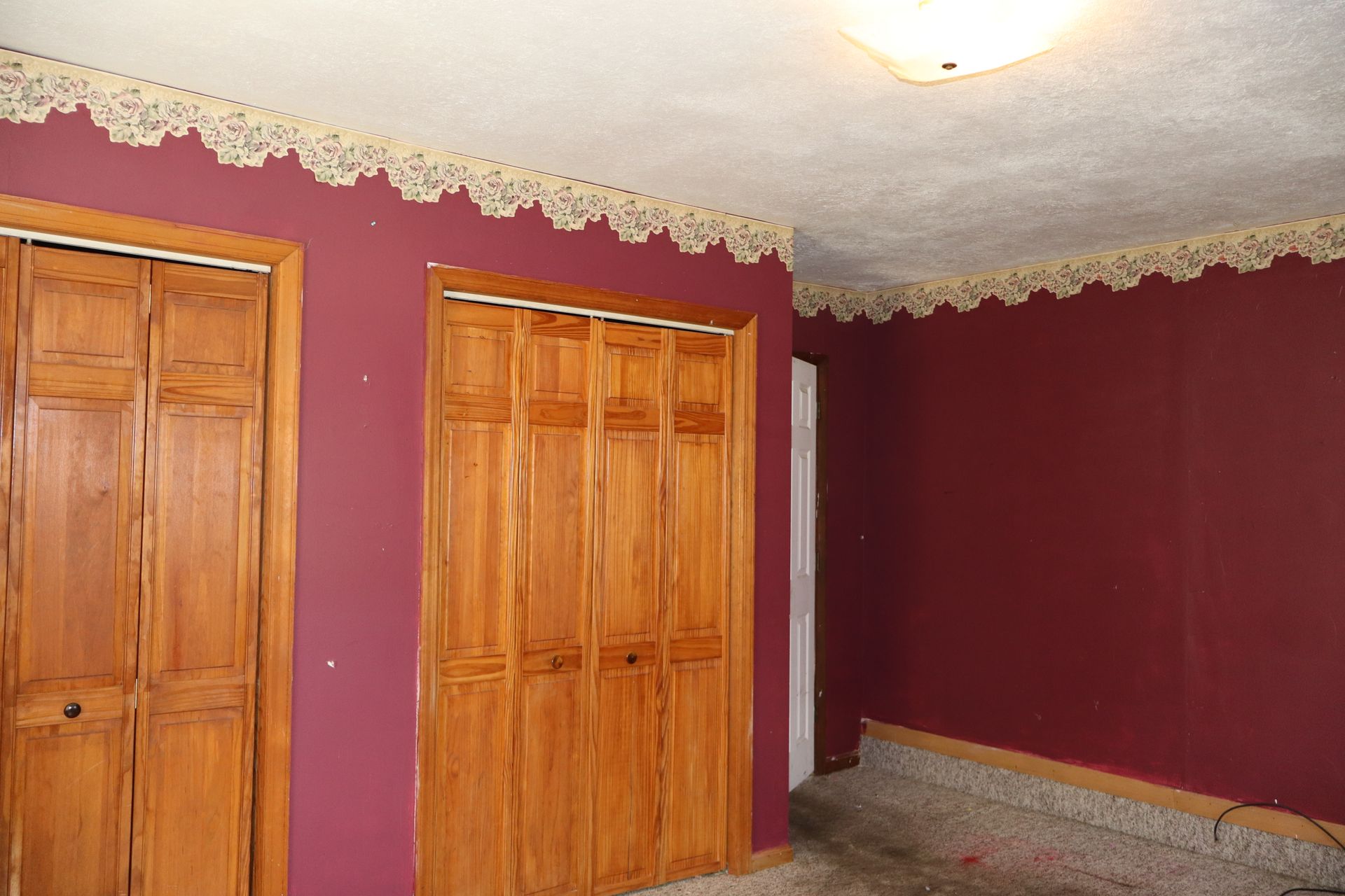 Maroon room with wood closets, lace trim near the ceiling, and a carpeted floor