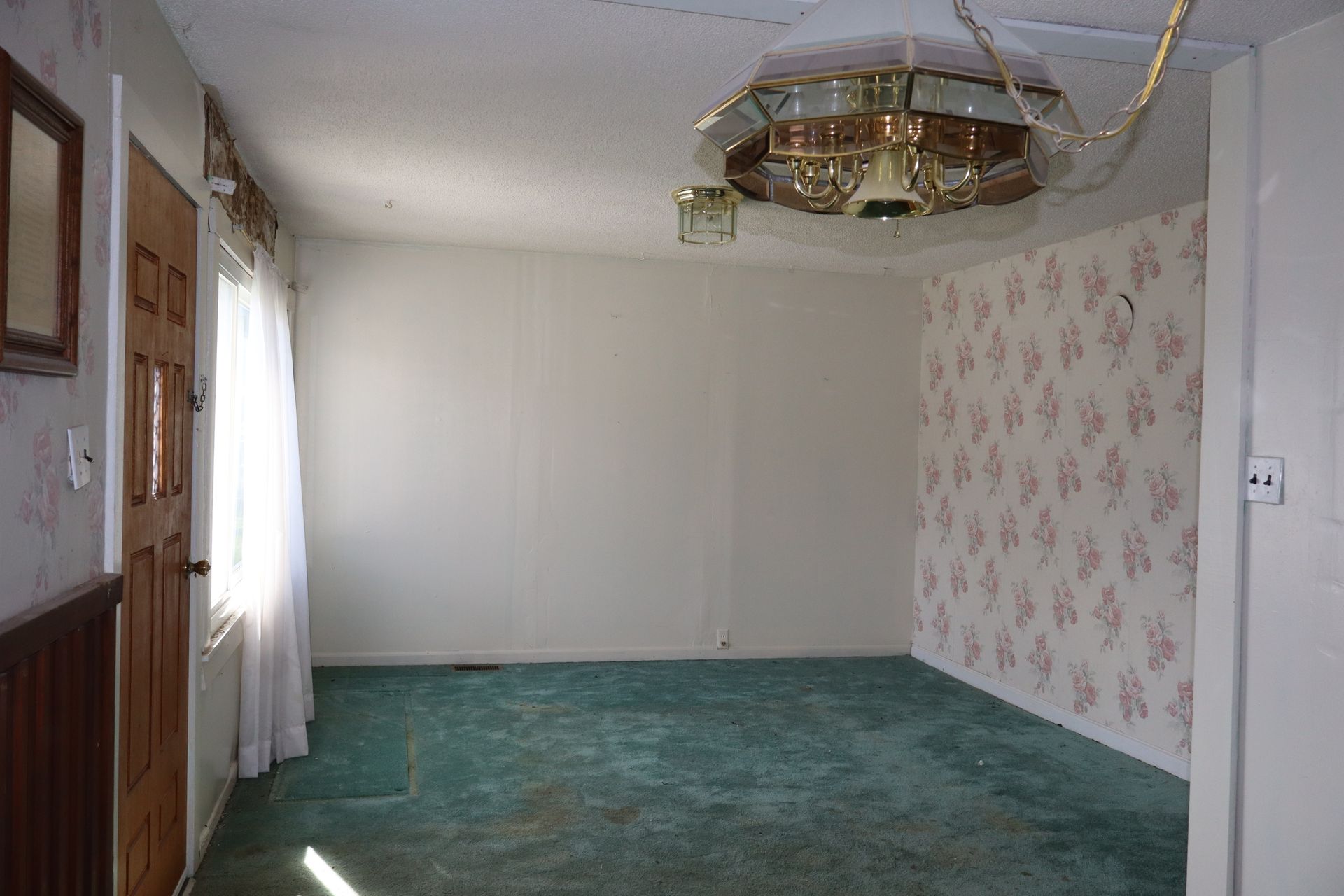 Empty room with green carpet, floral wallpaper accent wall, and ceiling light fixture.