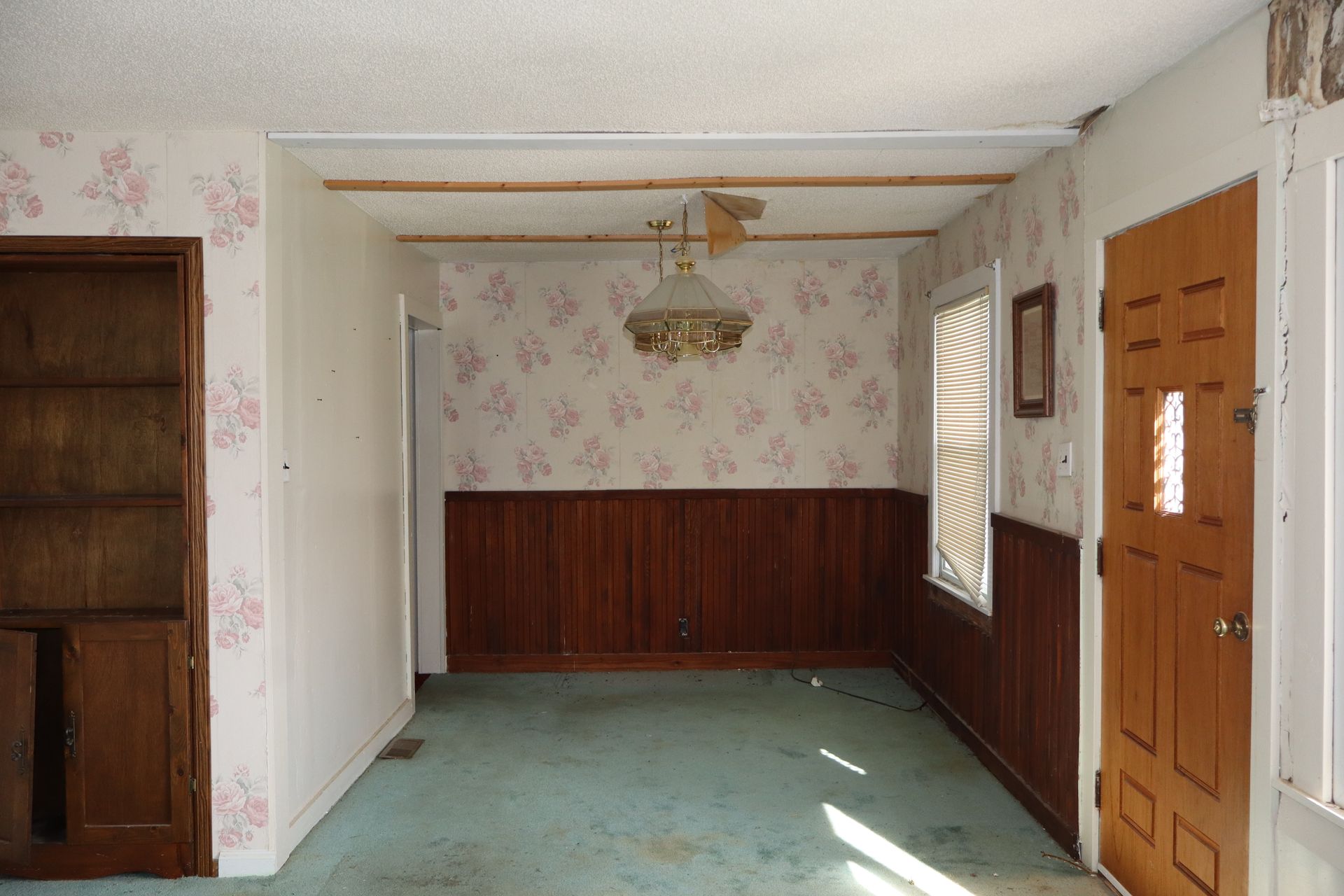 Empty living room with floral wallpaper, wood paneling, green carpet, and a ceiling fan