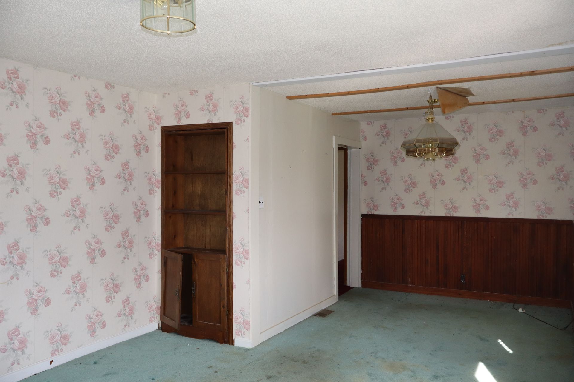 Empty room with floral wallpaper, green carpet, and wooden paneling and doors.