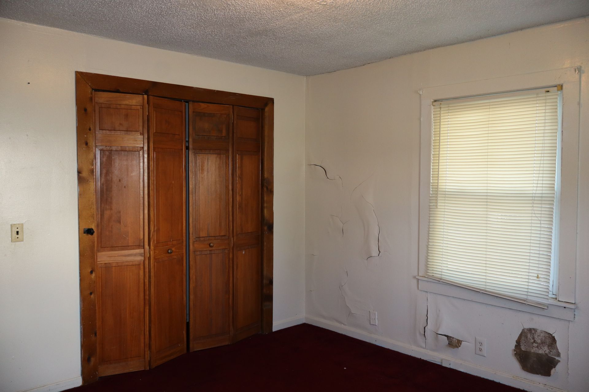 Empty bedroom corner with wooden closet doors and a window with blinds.