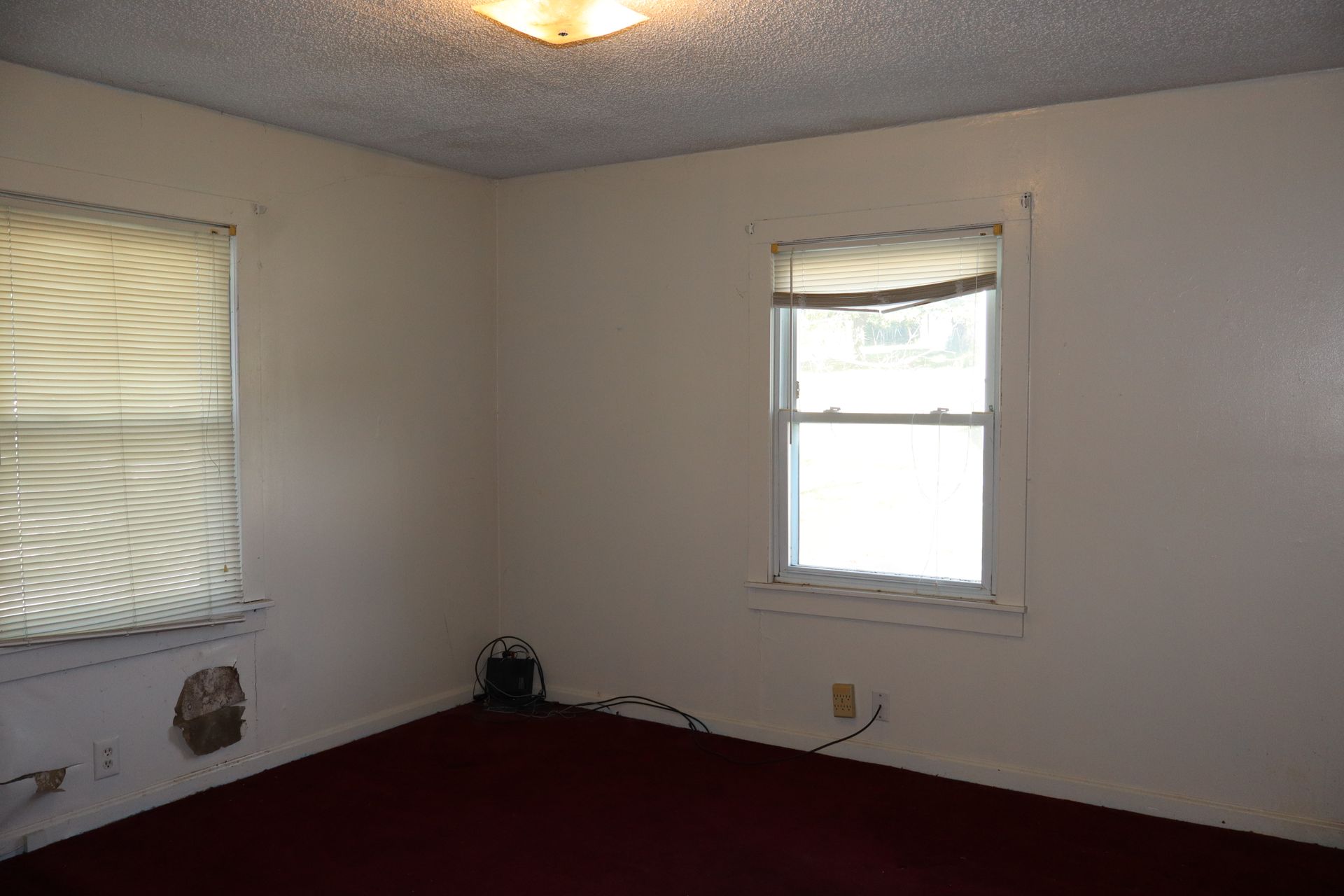 Empty beige room with two windows, red carpet, and ceiling light