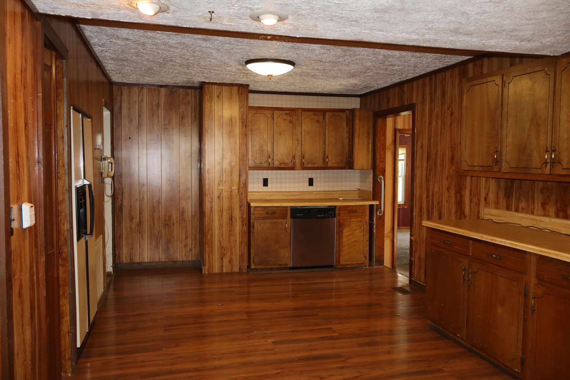 Empty wood-paneled kitchen with hardwood floors, cabinets, and a stove beneath a windowed counter.