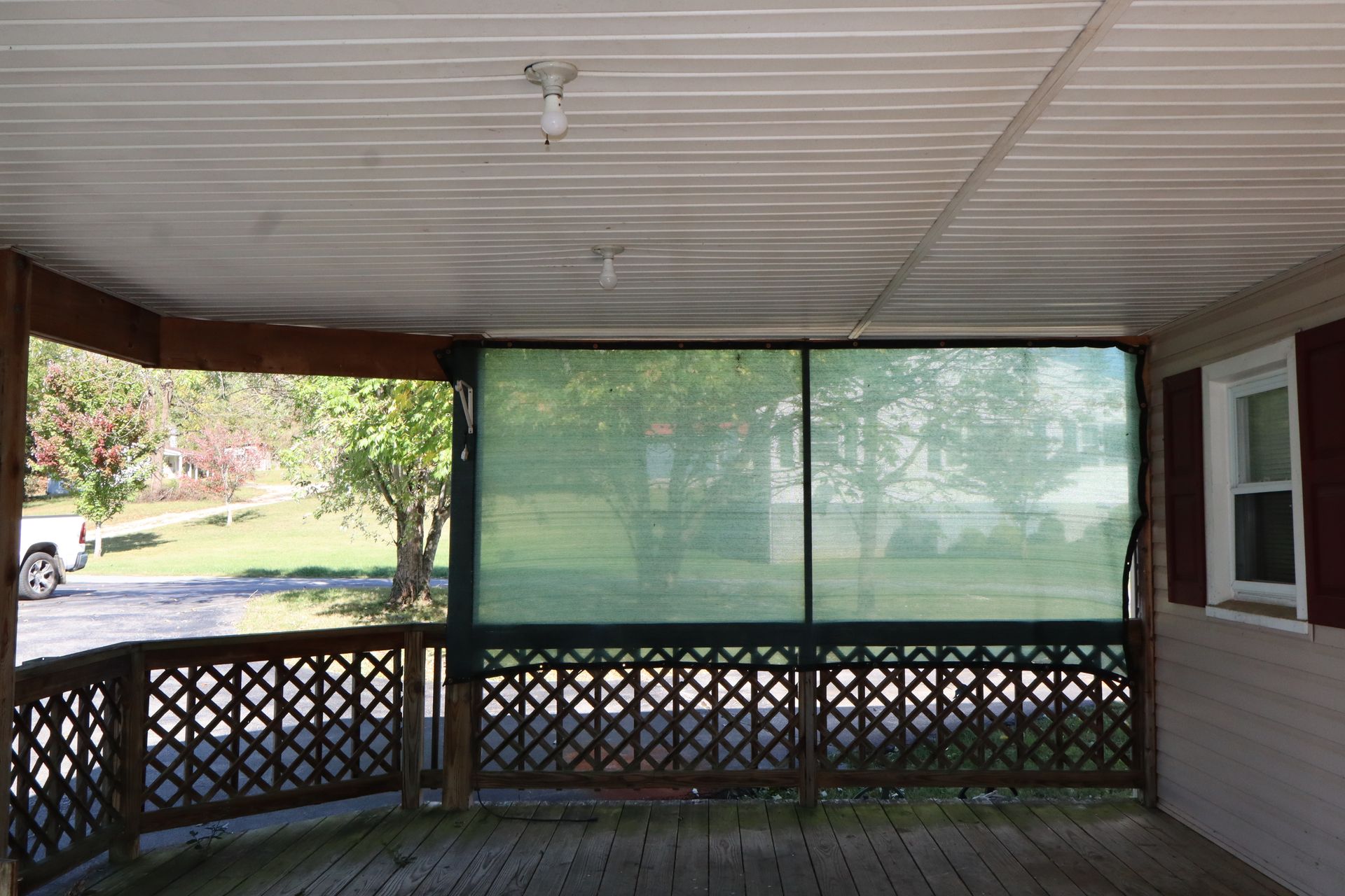Covered porch with lattice railing, green sun shades, and a view of a yard beyond