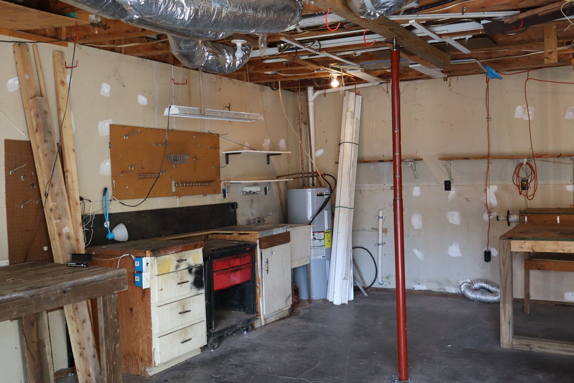 Partially gutted garage with exposed ceiling, workbench, cabinets, and a red support pole
