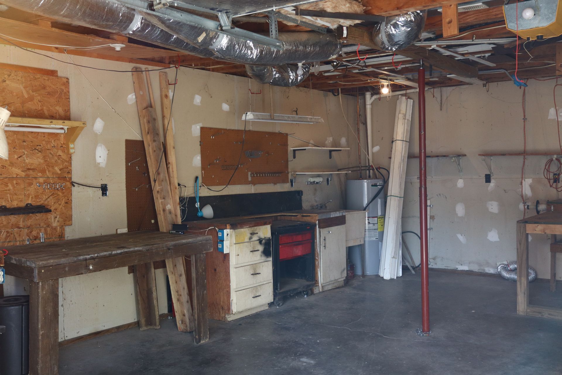 Cluttered unfinished garage with workbench, cabinets, exposed ceiling, and concrete floor