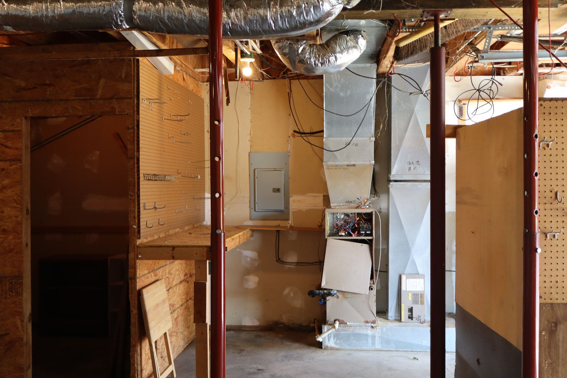 Unfinished basement with exposed wood framing, ductwork, and a small gray utility door.