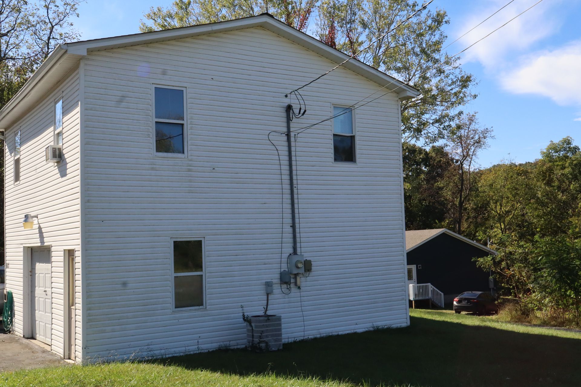 White two-story house with white siding, small windows, and a grassy yard under a blue sky.