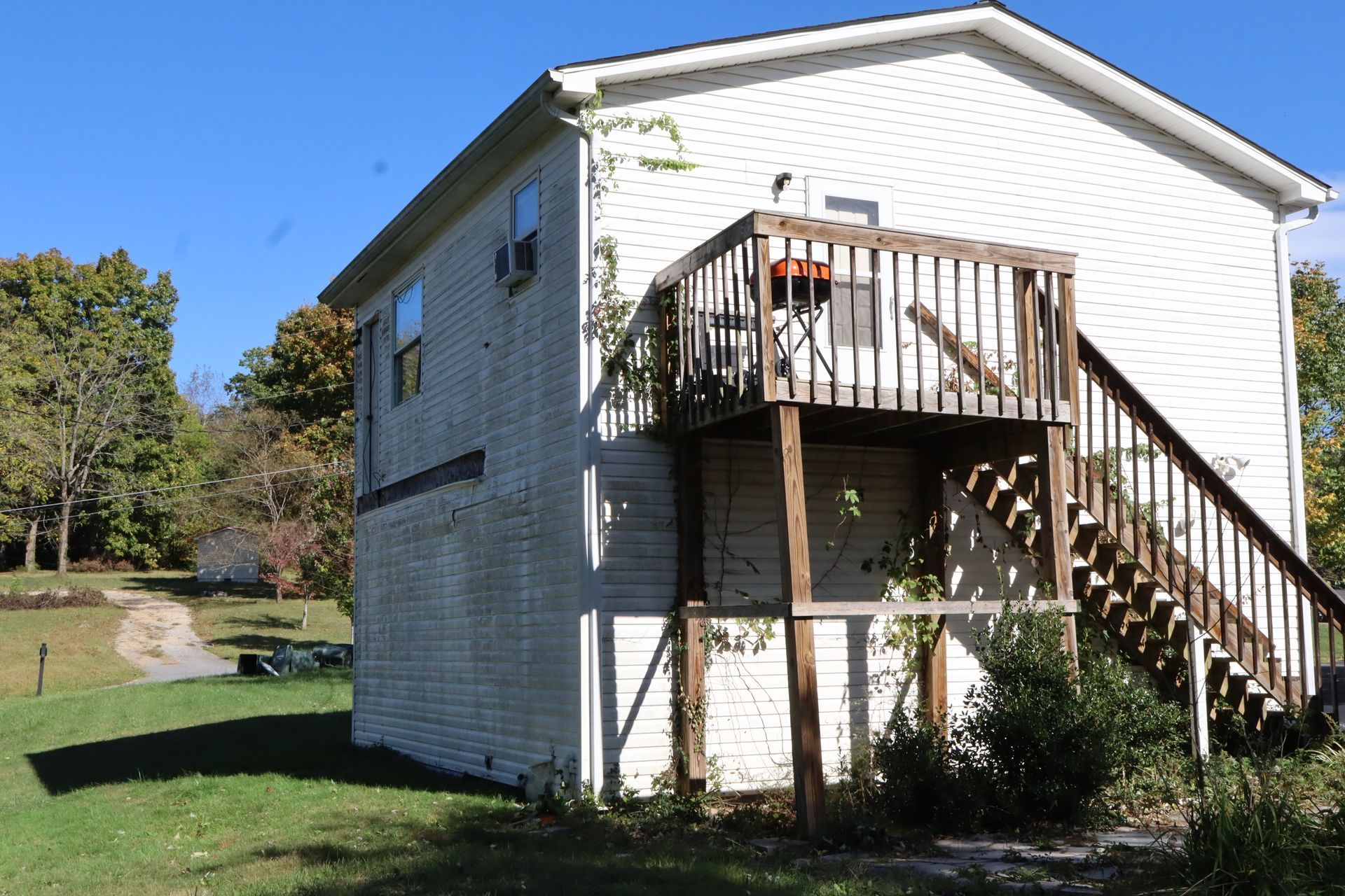 White two-story house with an exterior staircase and small deck in a grassy yard.