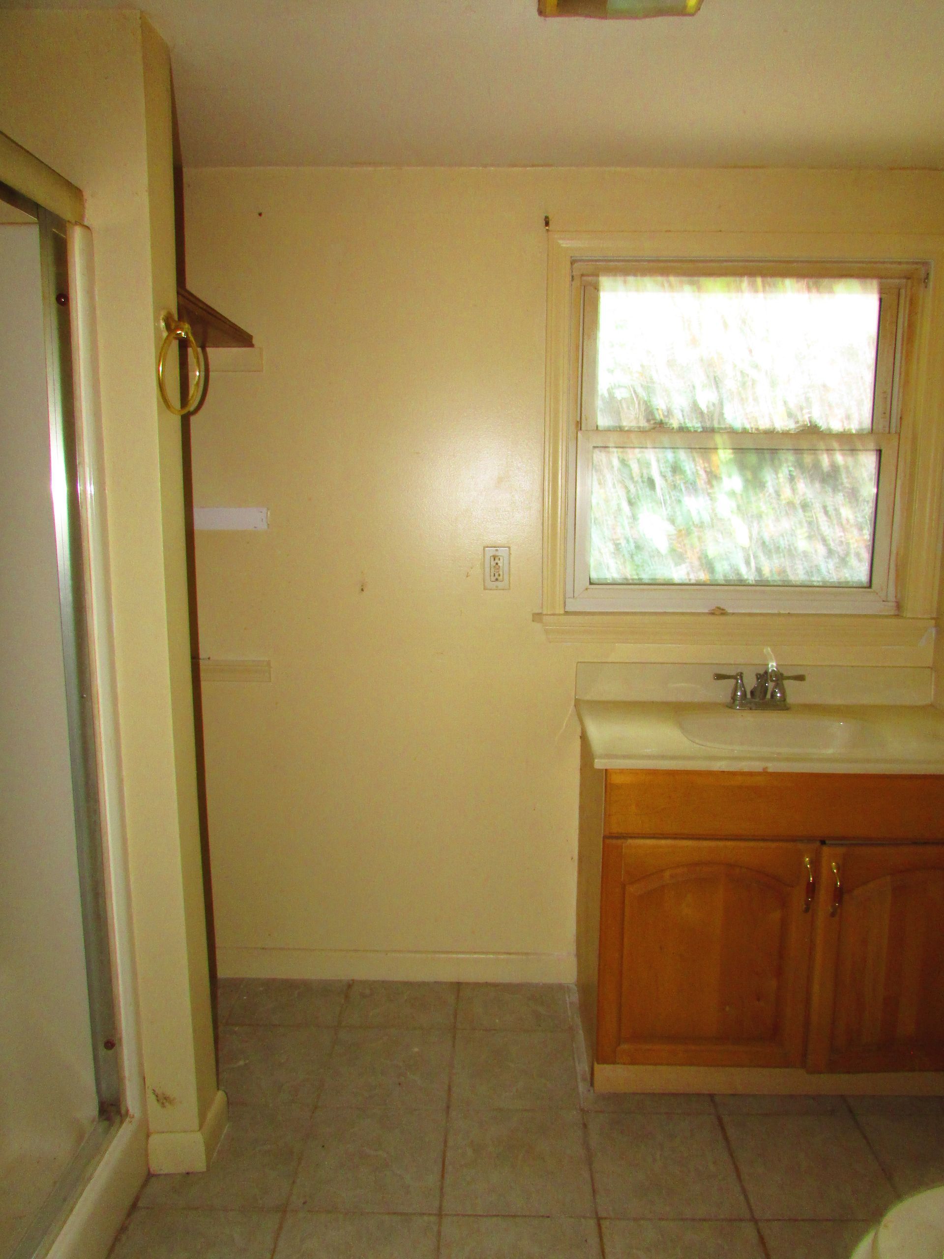 Bathroom interior with shower, vanity, window, and tile floor; beige walls.