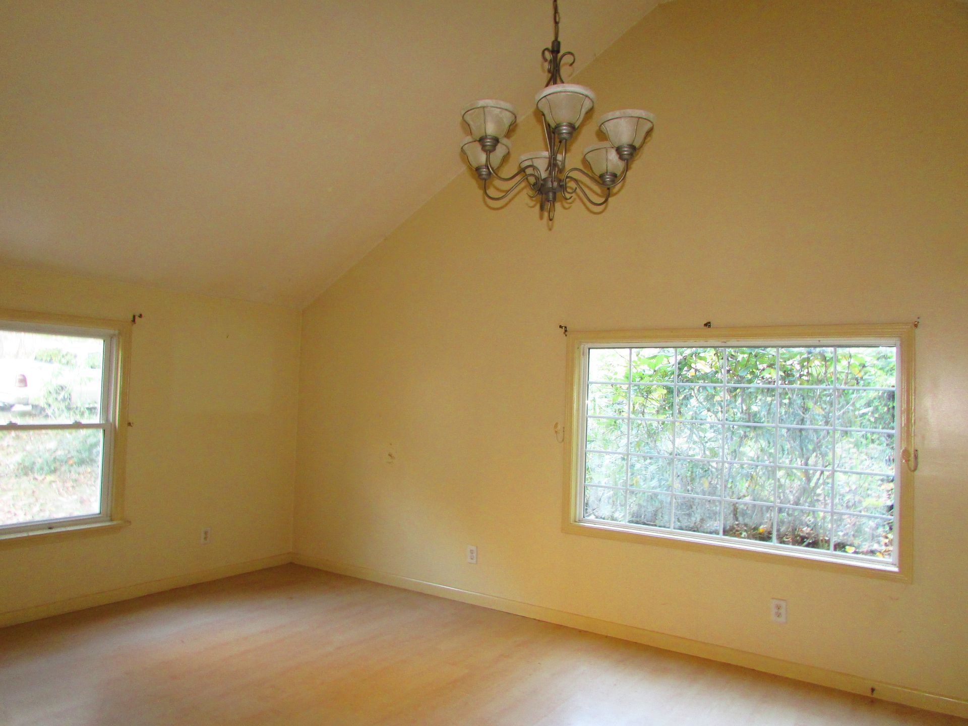 Empty room with light yellow walls, vaulted ceiling, two windows, and chandelier.