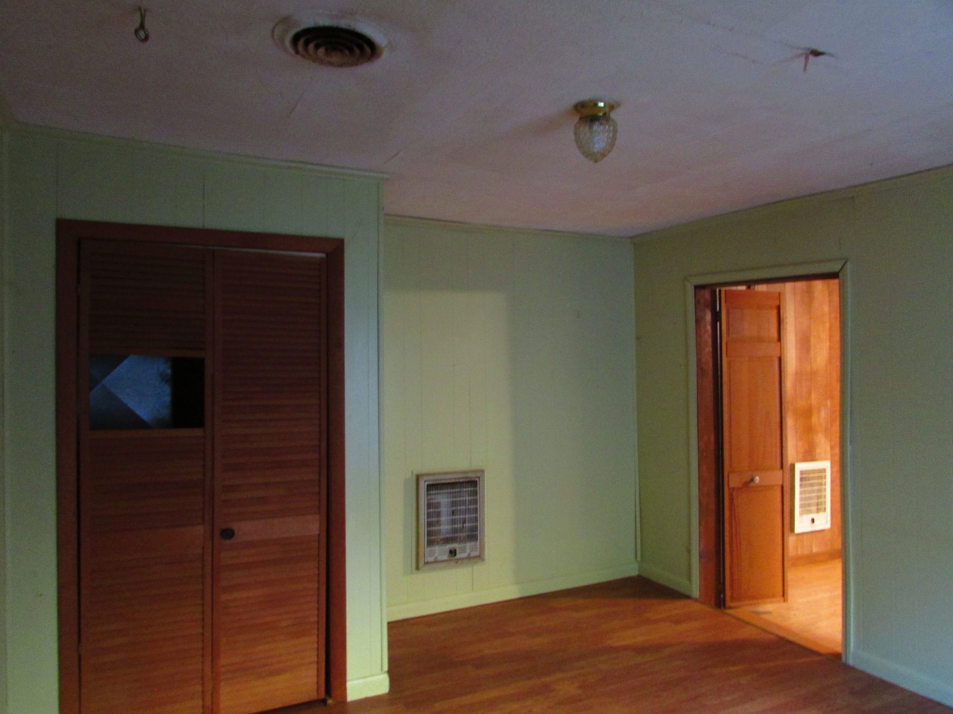 An empty room with light green walls, wood floors, and closed wooden closet doors.
