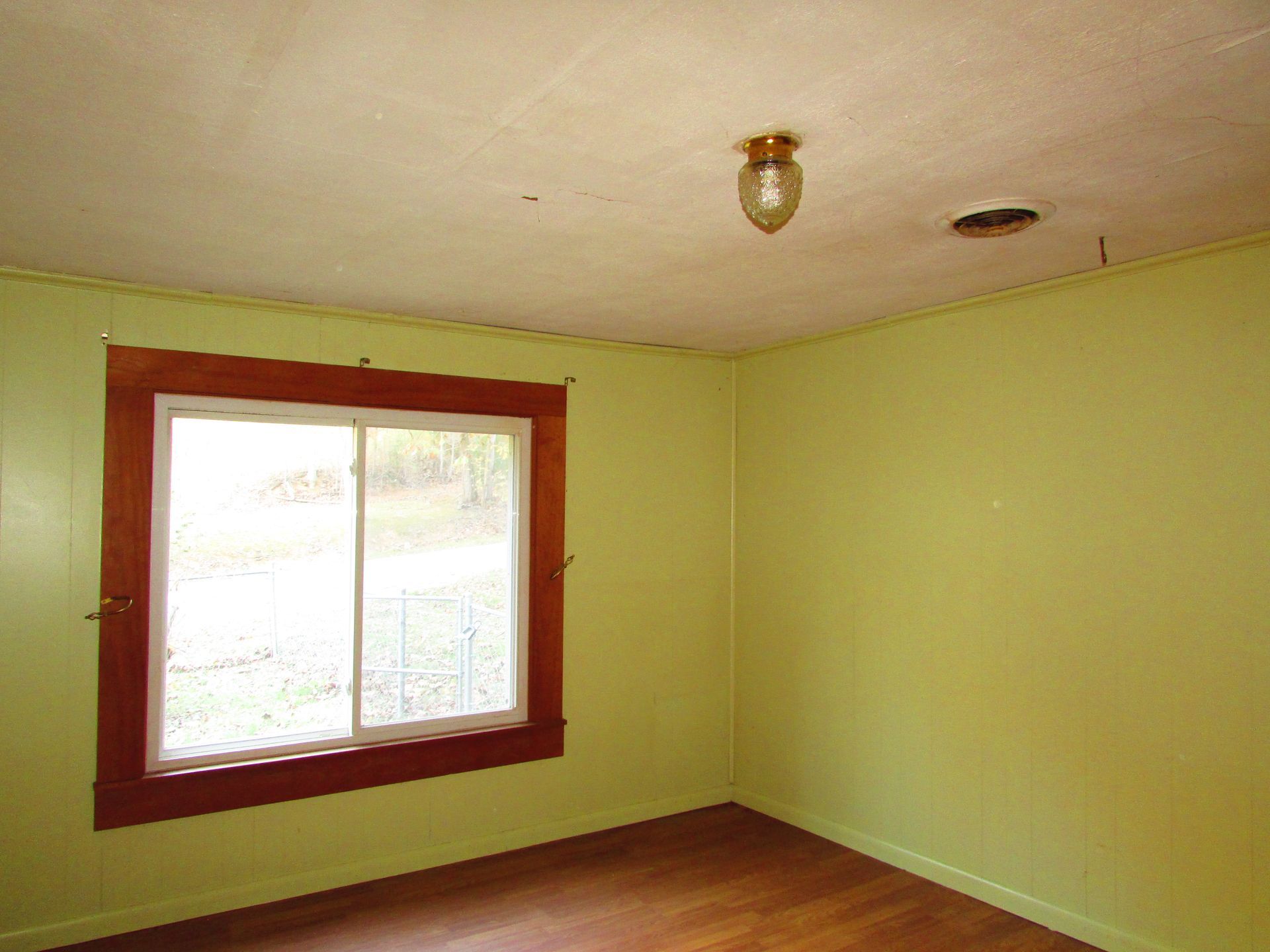 Empty room with a window and a light fixture; walls are green, window frame is brown.
