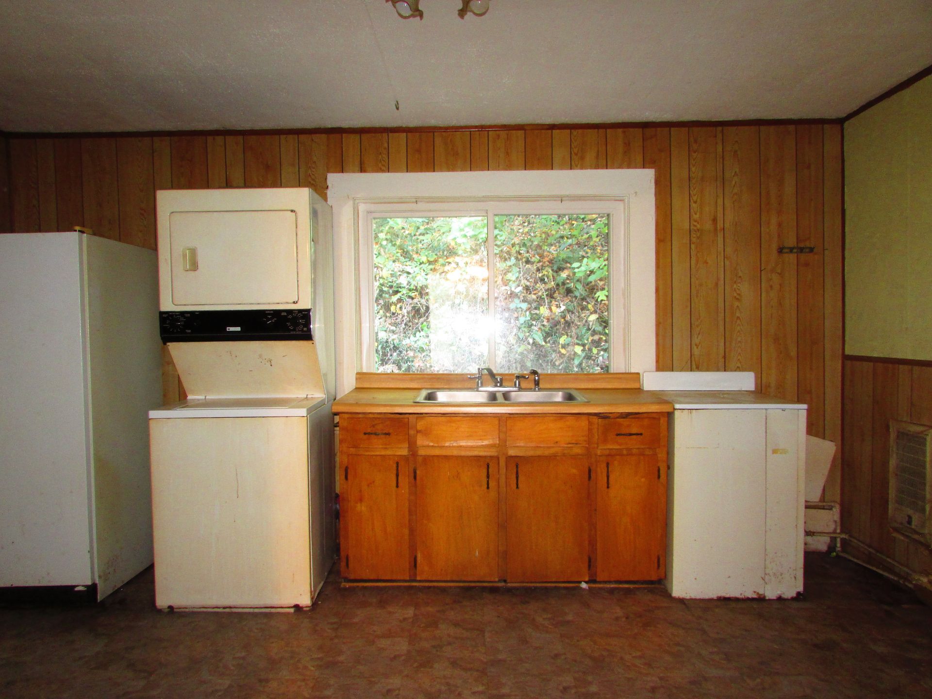 A kitchen with a window, wooden cabinets, and appliances like a washer, dryer, and refrigerator.