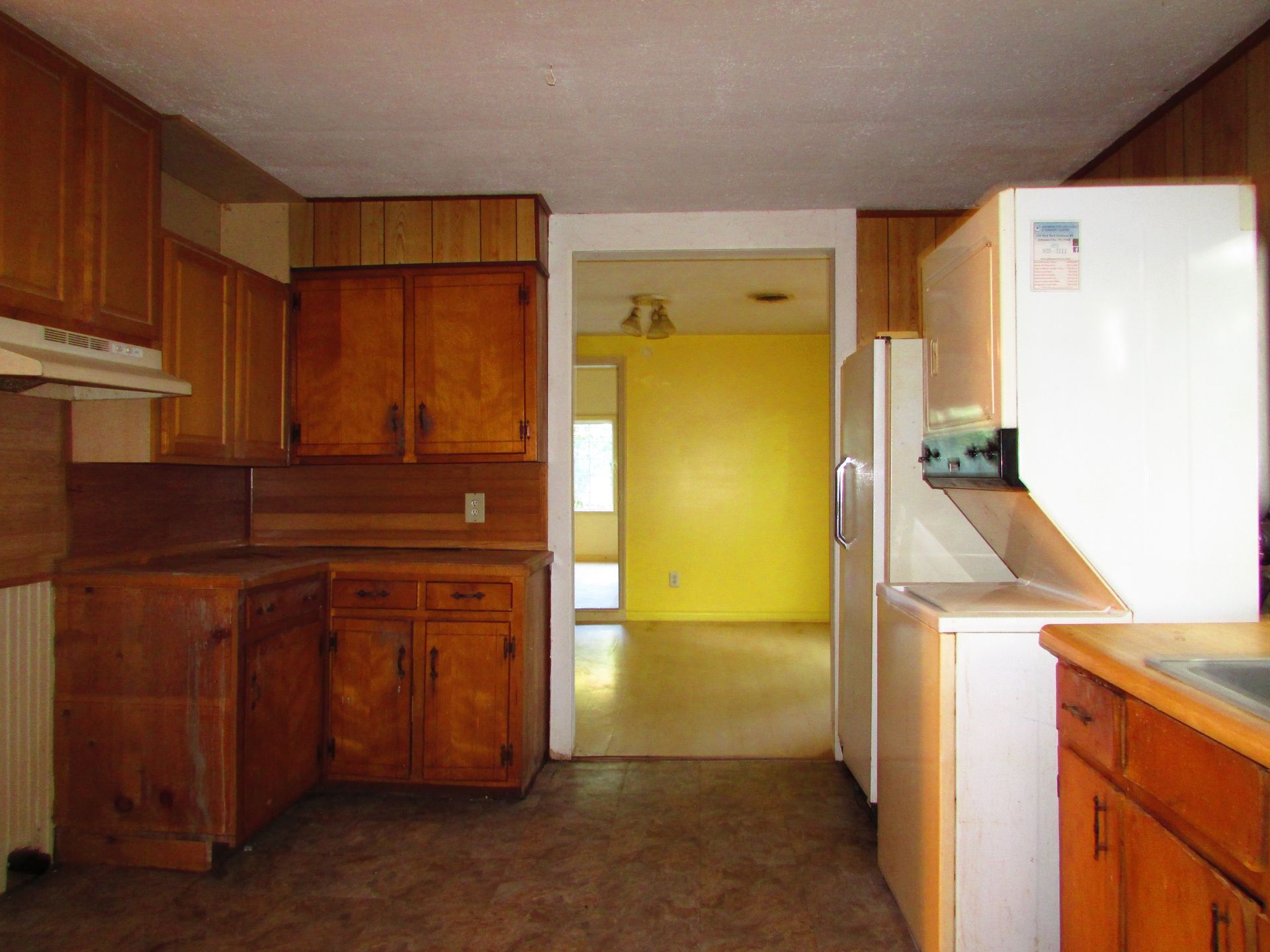Kitchen with wooden cabinets, refrigerator, and doorway to a yellow-walled room.