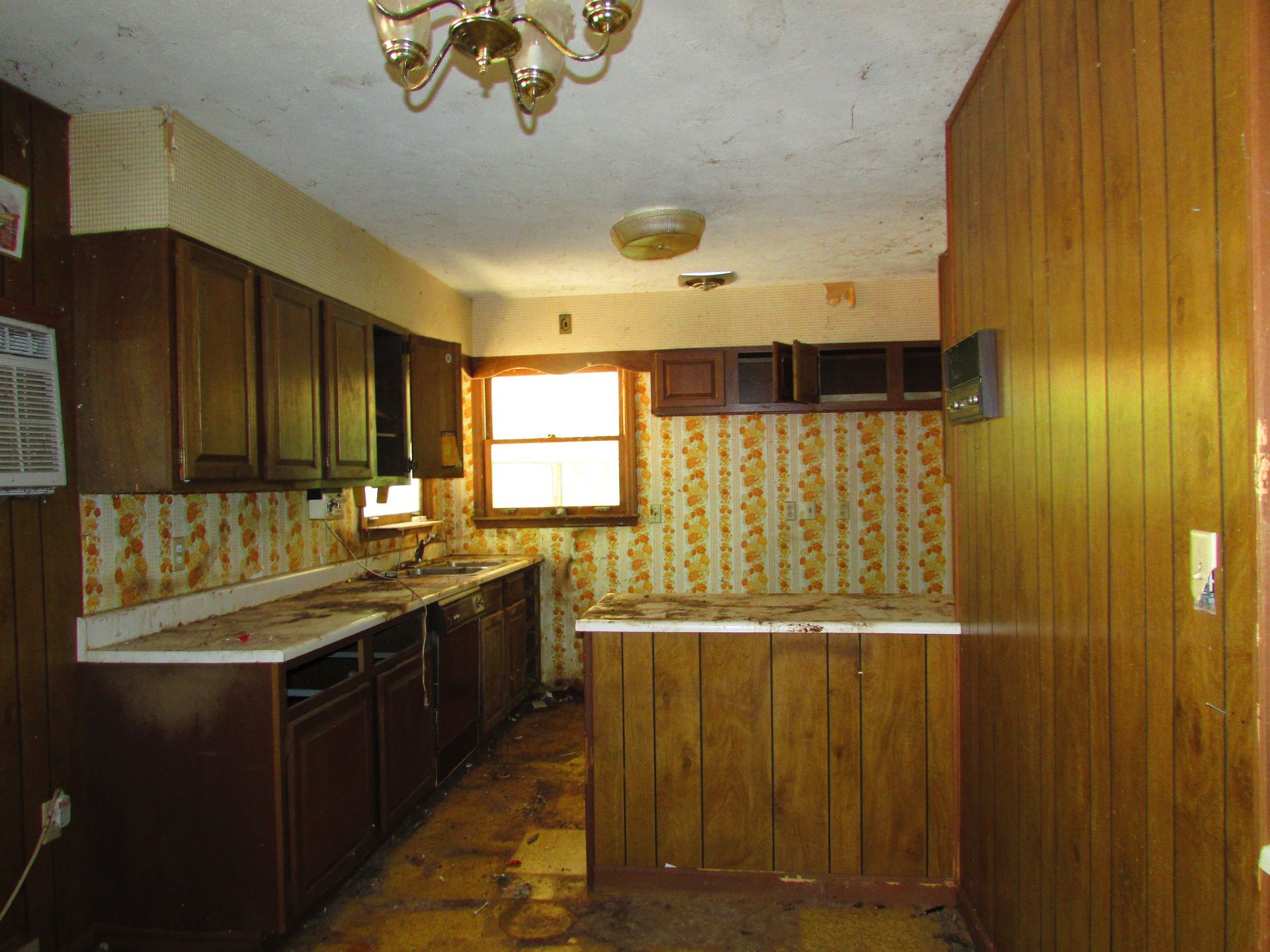 Vintage kitchen with dark wood cabinets, floral wallpaper, and a window over the sink.