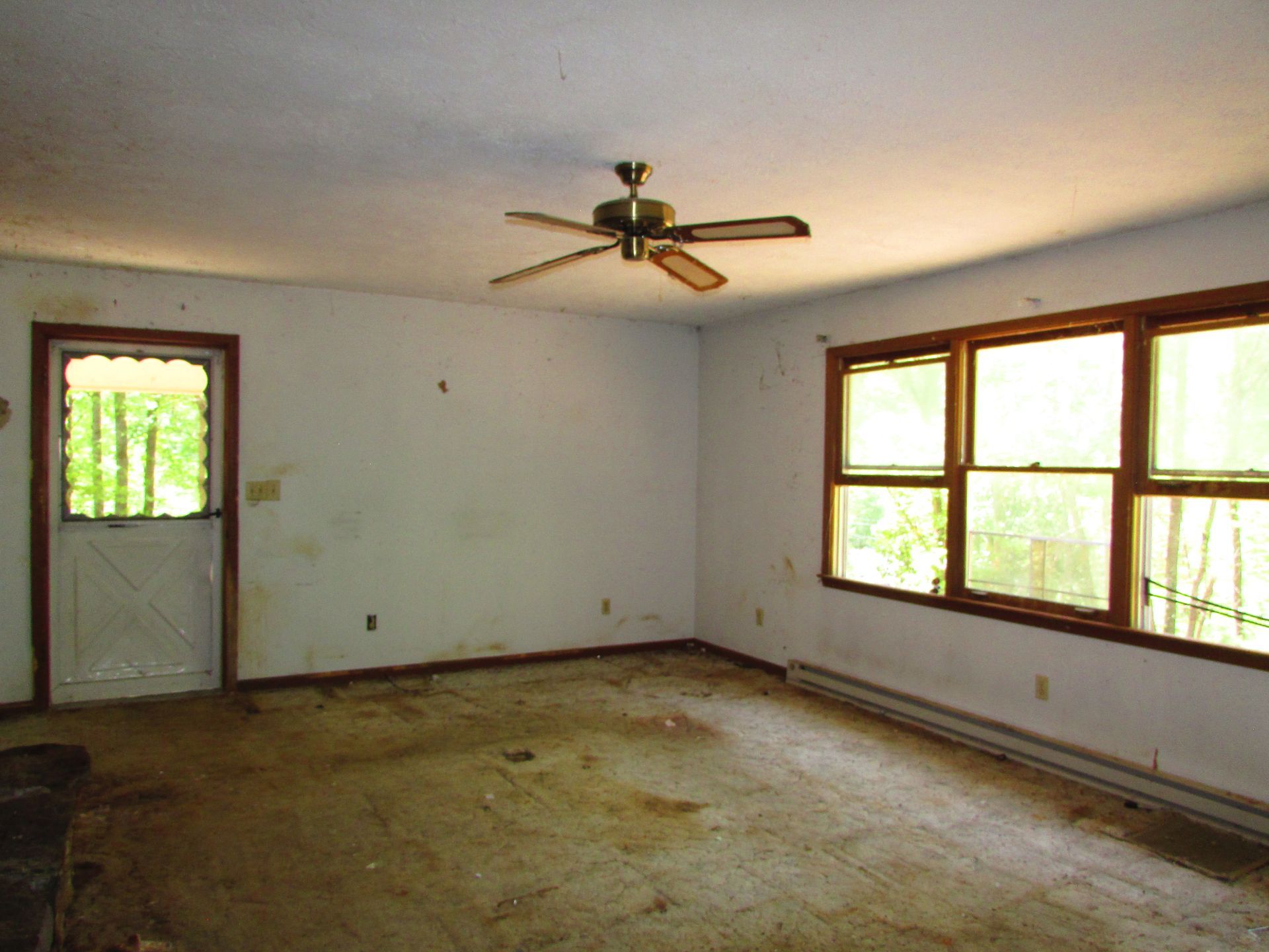 Empty room with worn carpet, ceiling fan, front door, and large windows letting in daylight