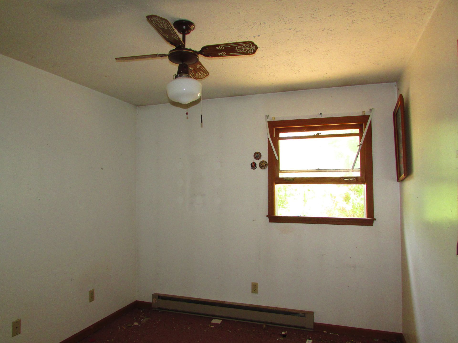 Empty room with white walls, wood floor, ceiling fan, and a small window letting in daylight