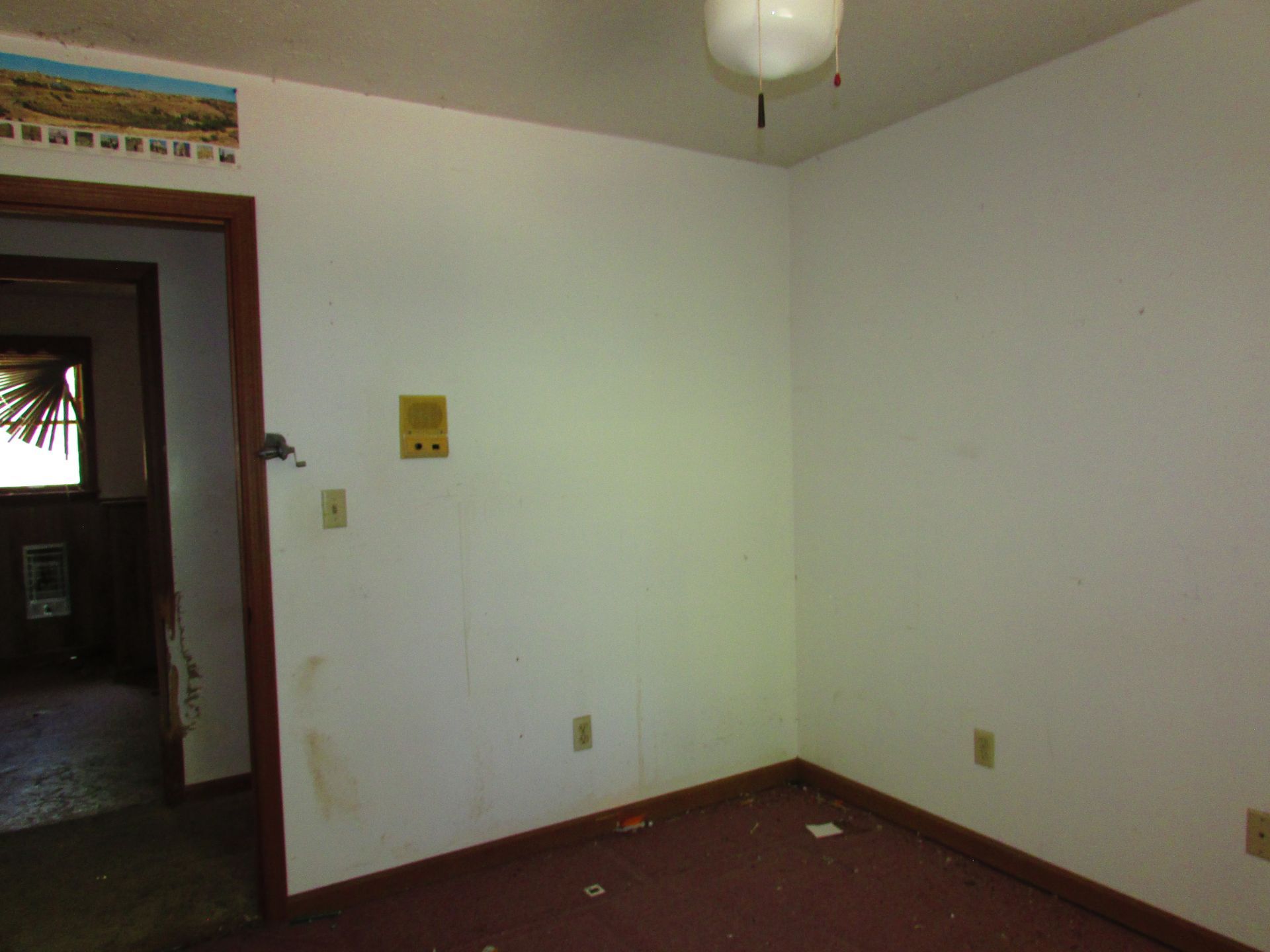 Empty room with white walls, maroon carpet, a ceiling light, and an open doorway to a darker hall