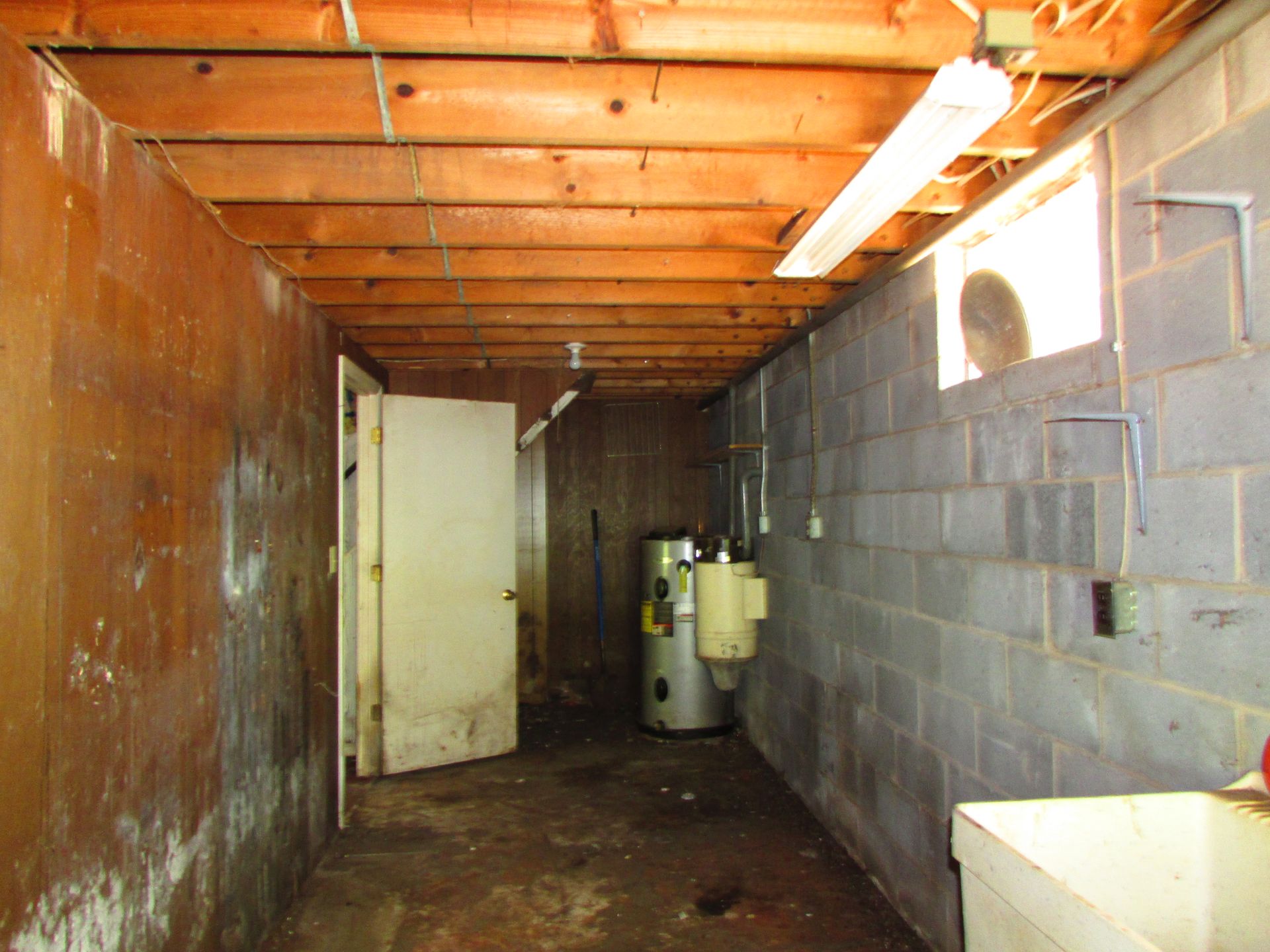 Narrow basement with cinder block walls, exposed ceiling beams, old appliances, and a white door in back