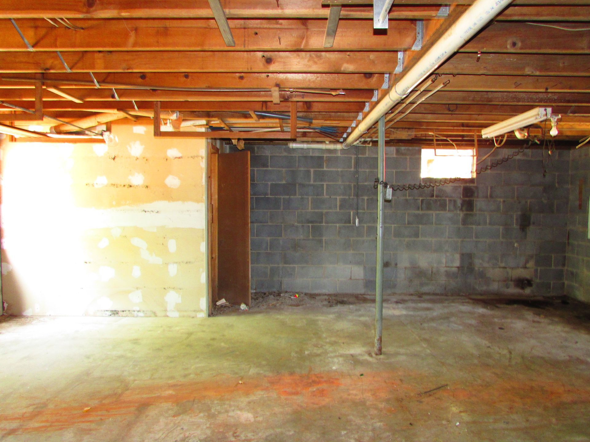 Empty unfinished basement with exposed beams, cinder block walls, and concrete floor