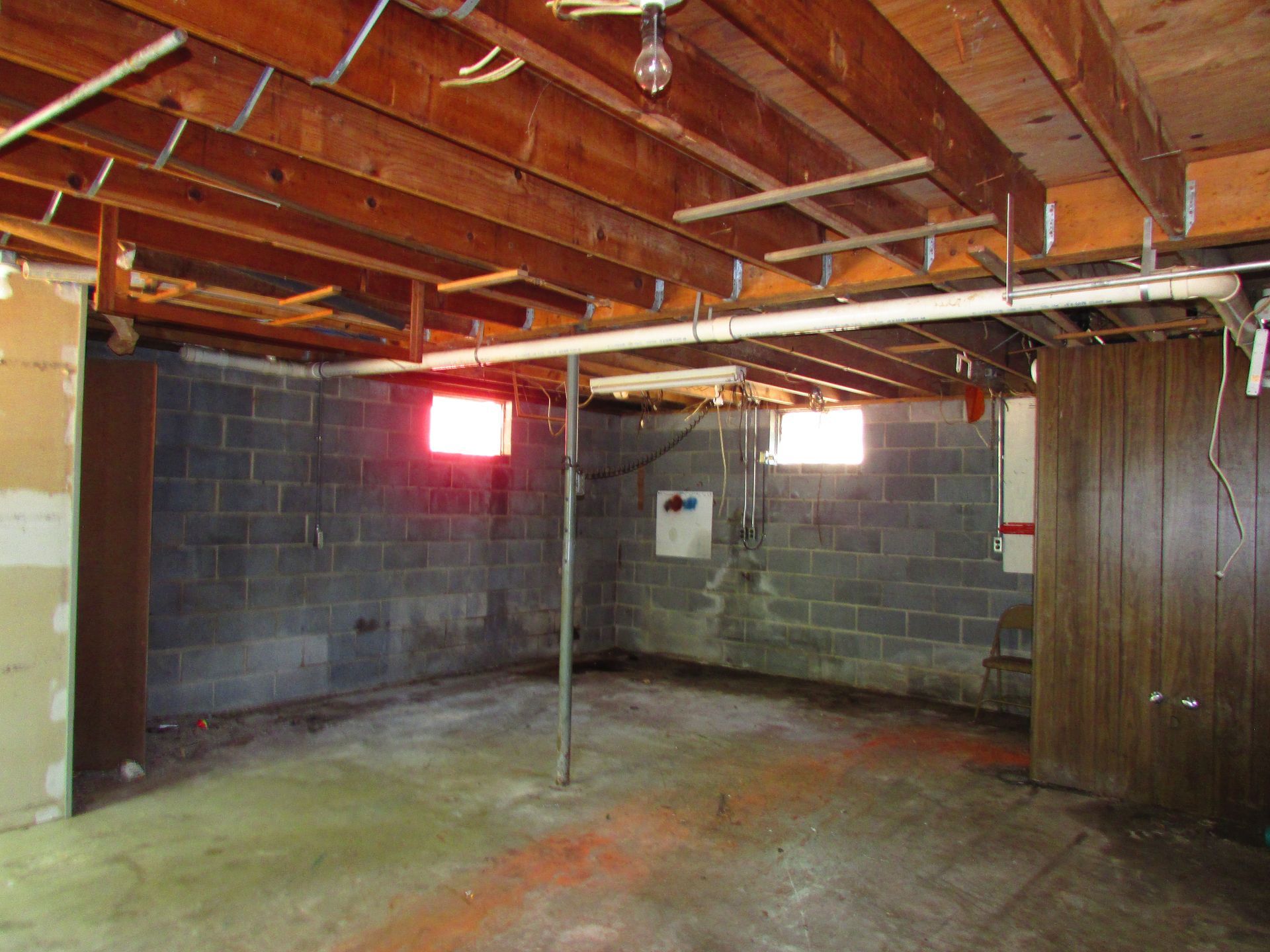 Bare basement with exposed ceiling joists, concrete block walls, and small windows