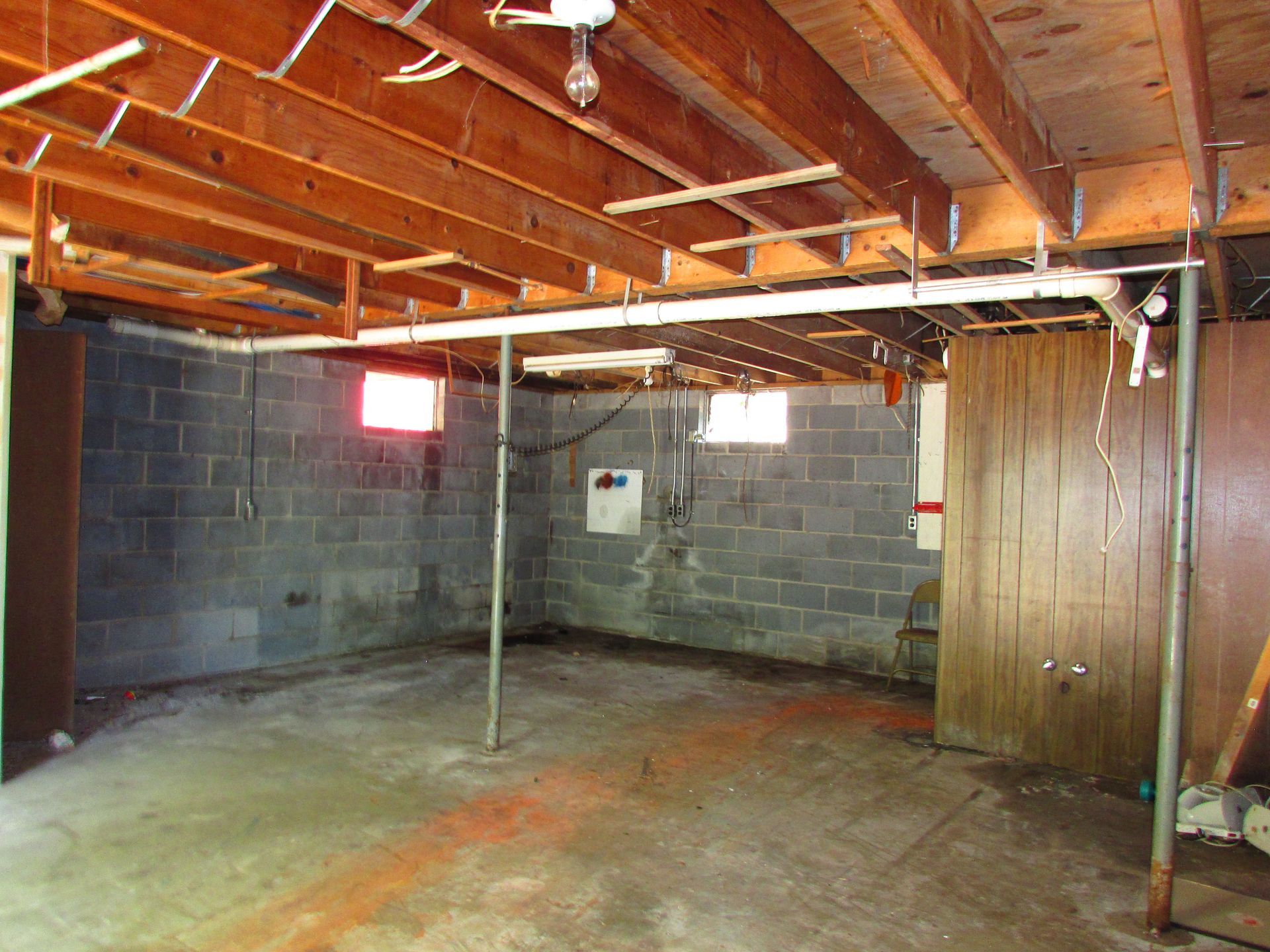 Unfinished basement with exposed wood joists, cinderblock walls, concrete floor, and a metal support pole
