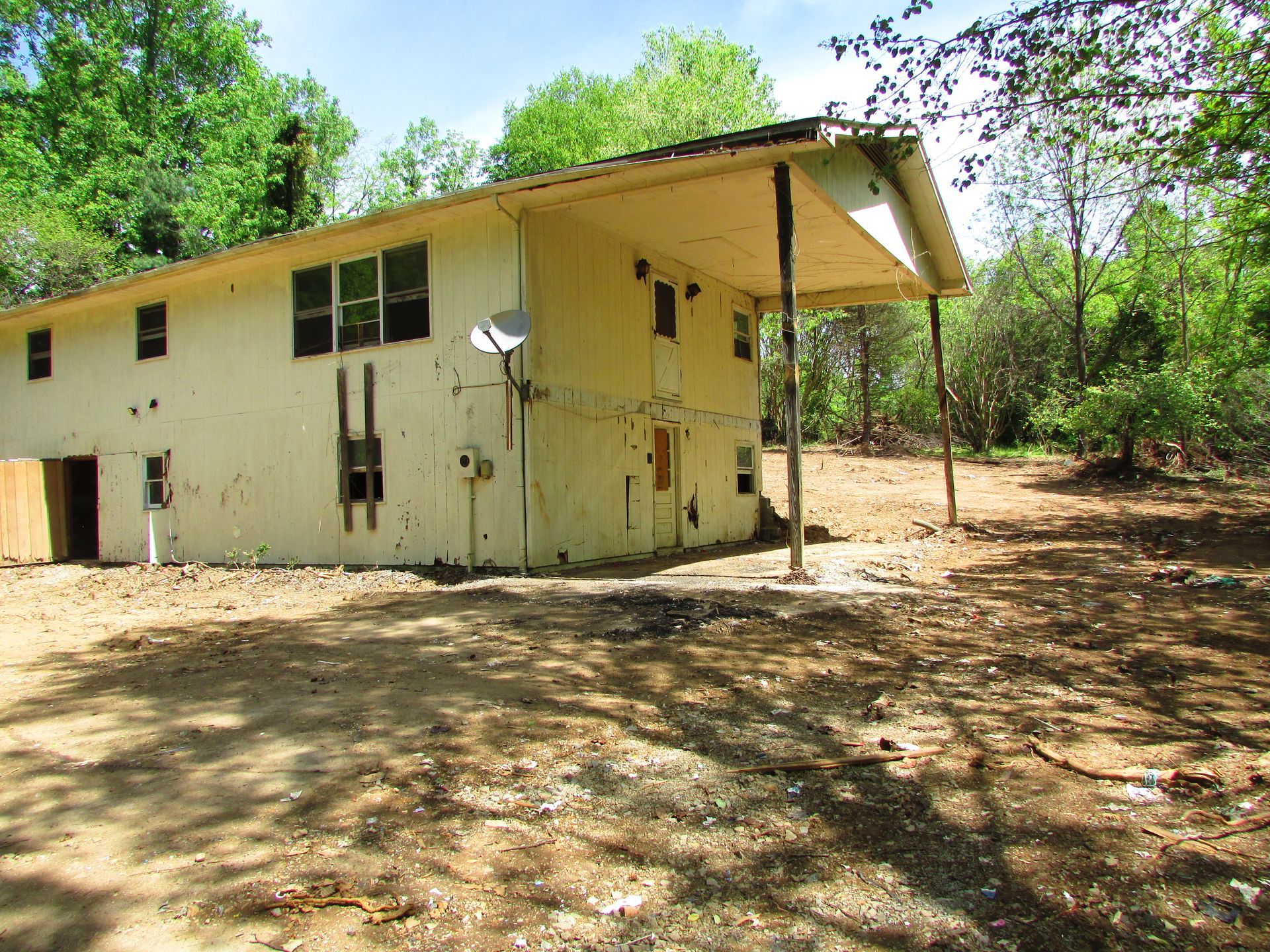 Small cream-colored house with a slanted roof in a wooded, sunlit clearing.