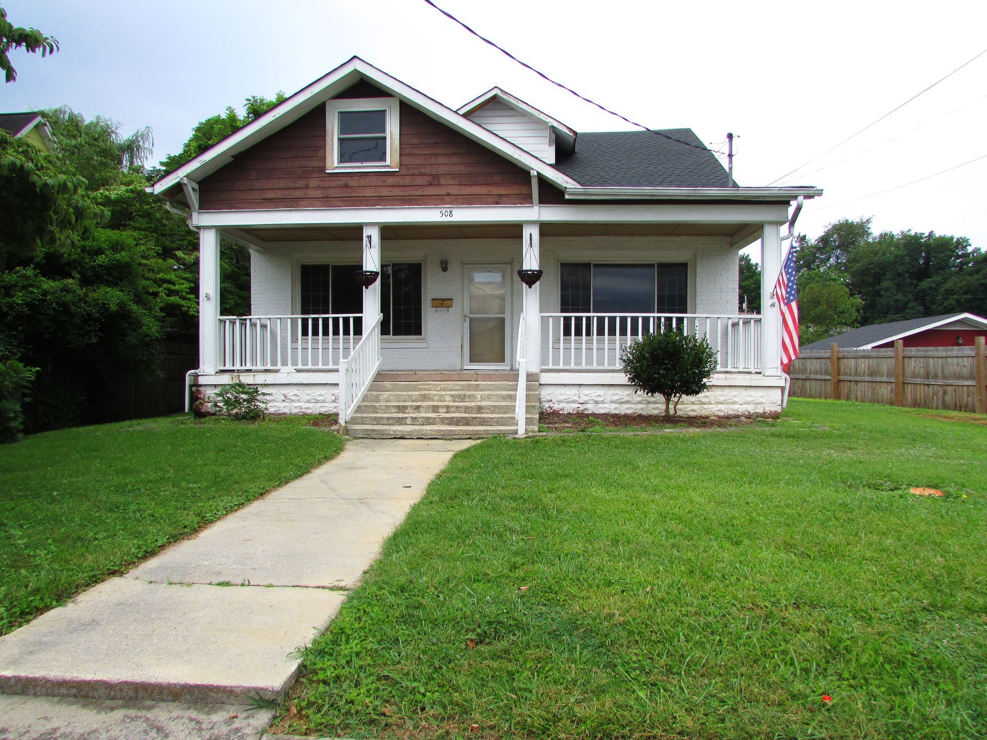 Small house with a front porch, white trim, green lawn, and a sidewalk leading to the entrance.