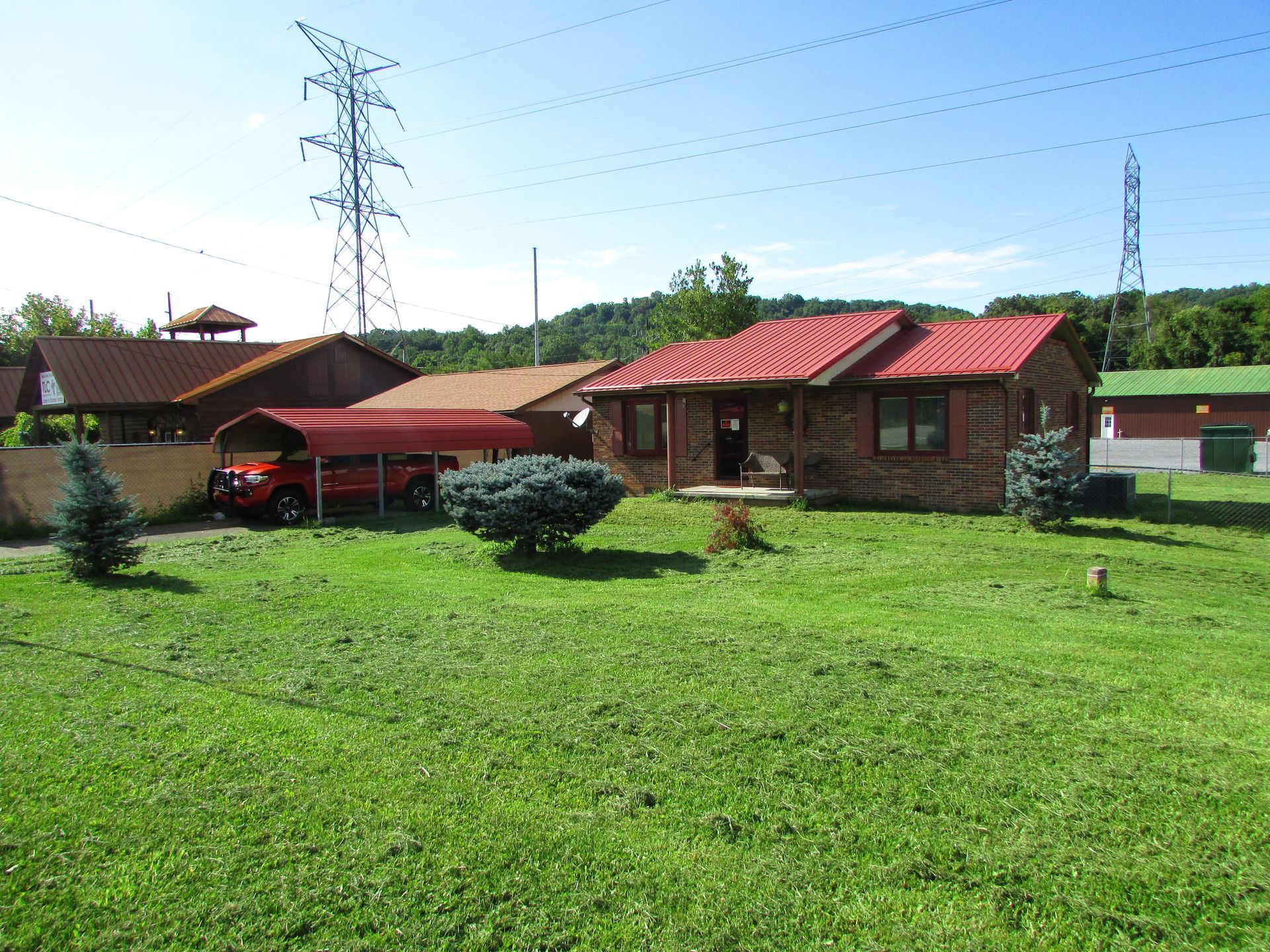 Rural house with red roof, parked red car, and green lawn under a clear blue sky