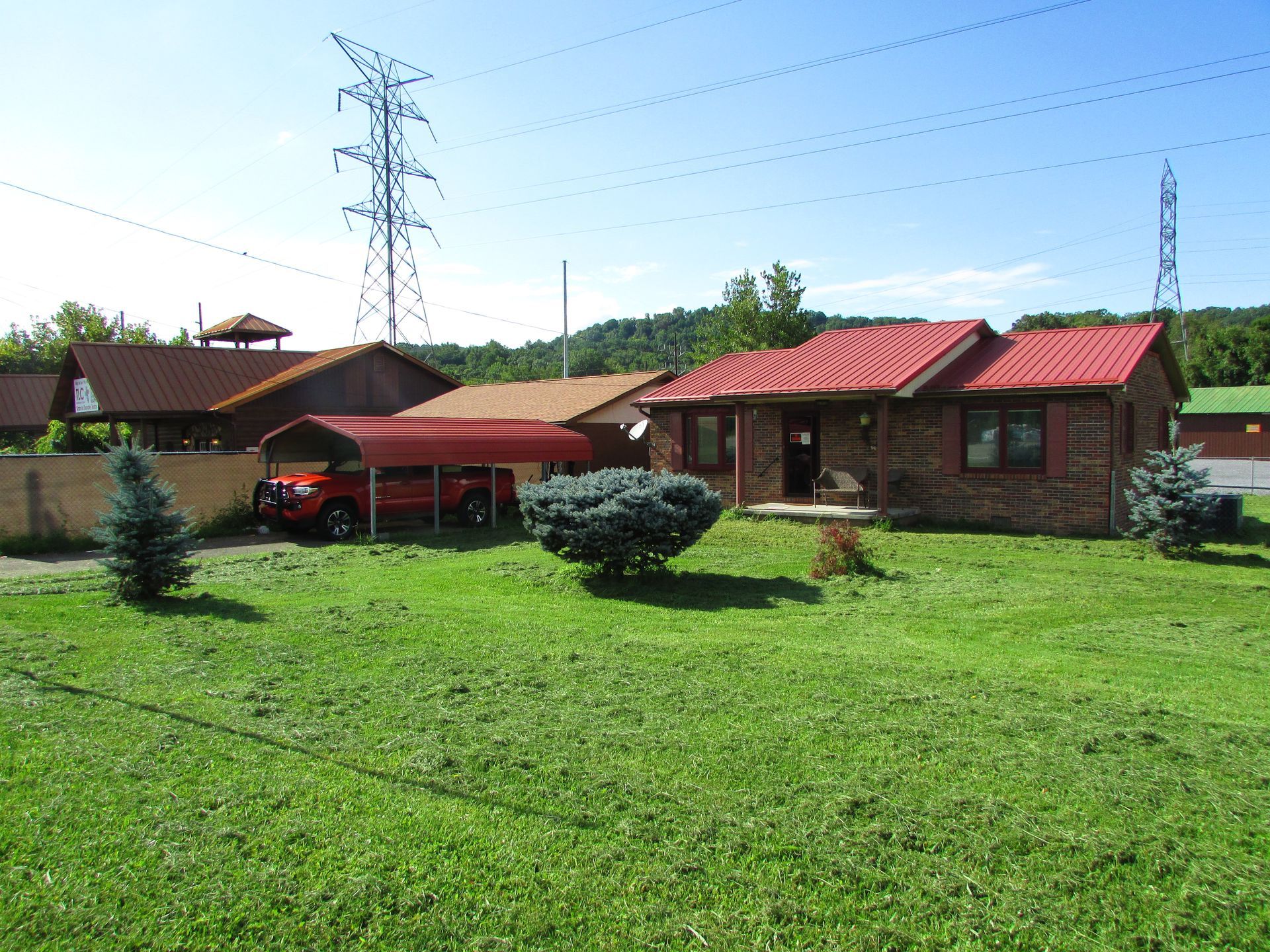 Suburban houses with red roofs, a red car under a canopy, and a green lawn in bright sunlight