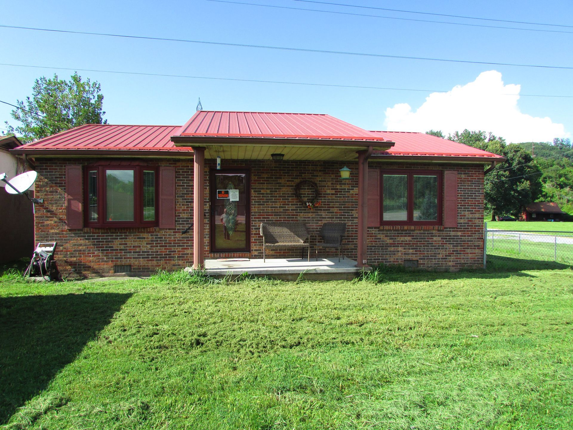 Small brick house with red metal roof and green lawn under a blue sky
